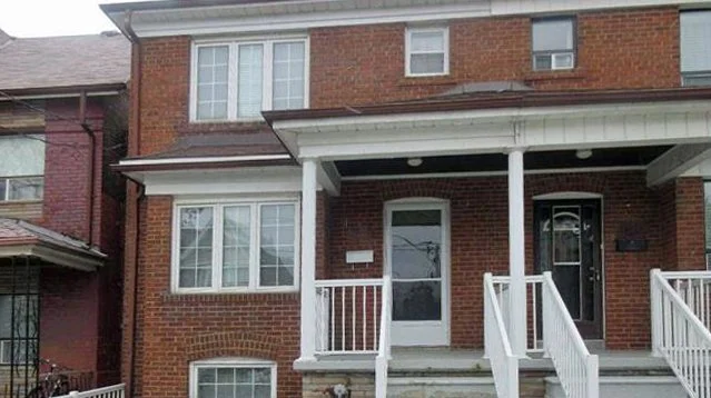 Front view of a brick residential building with stairs, a porch, and a door.