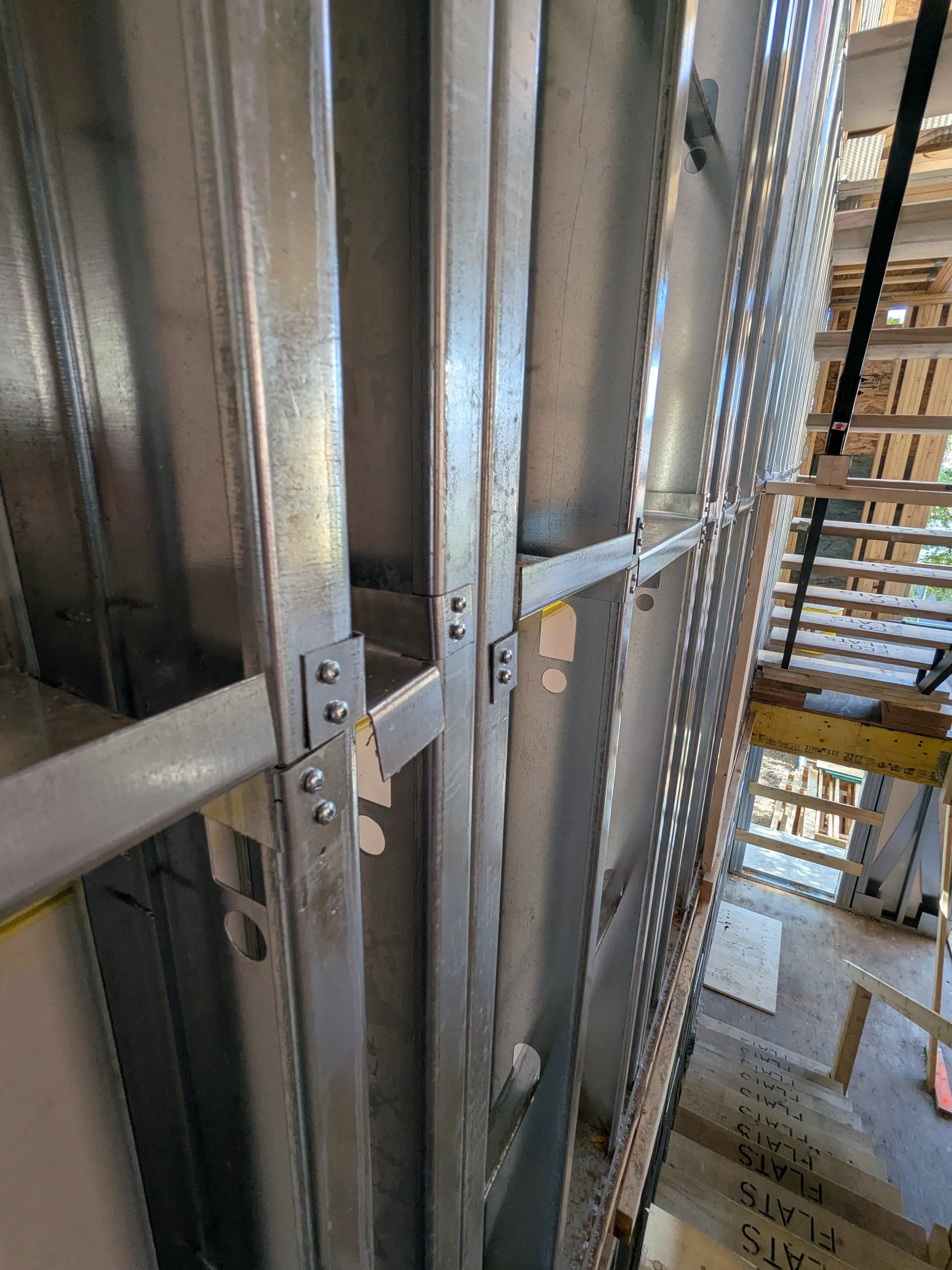 Close-up view of a steel-framed wall under construction at a building site, with wooden scaffolding and stairs visible in the background.
