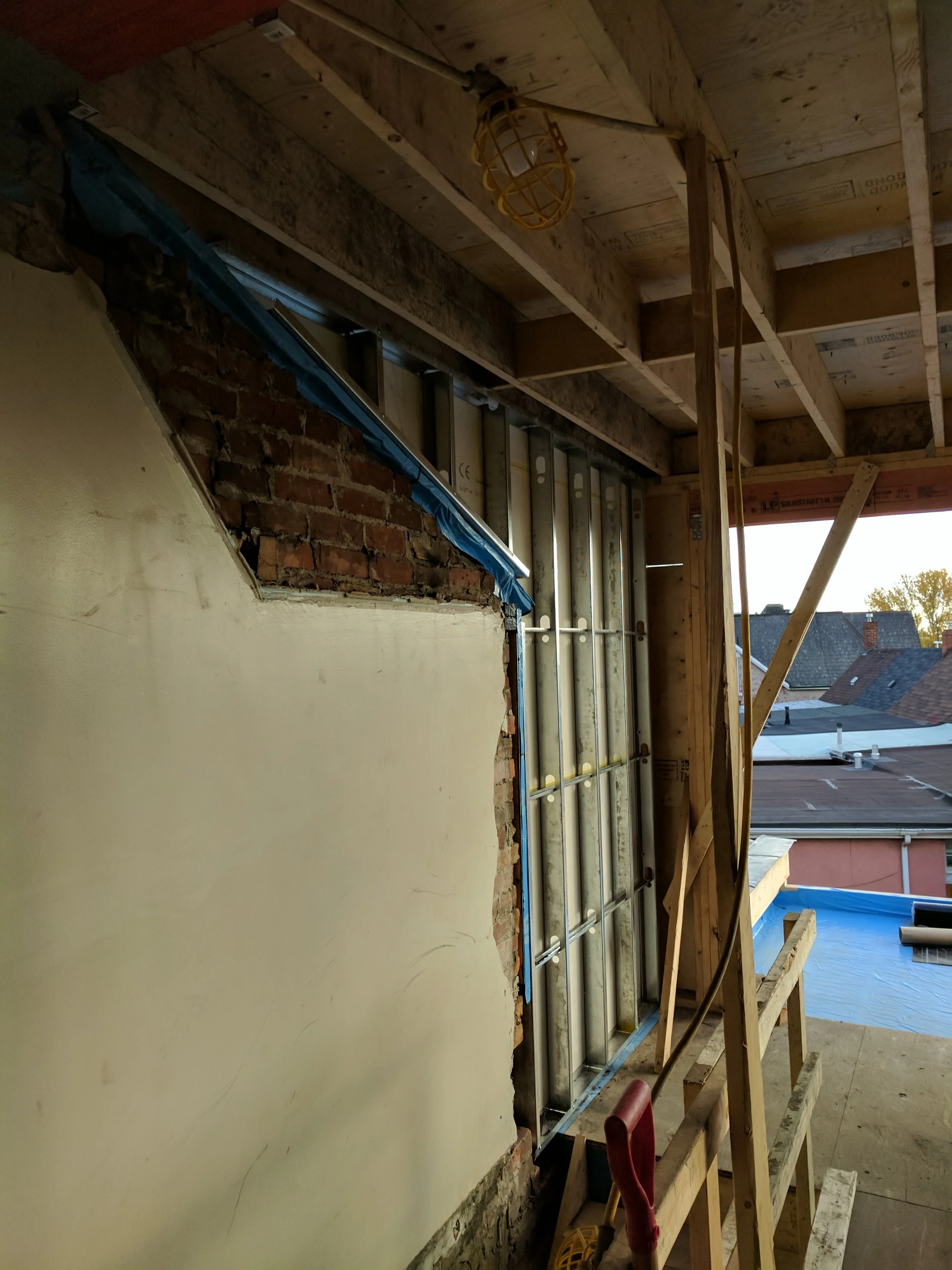 Construction site with exposed brick wall, wall framing, construction tools, and an unfinished ceiling.