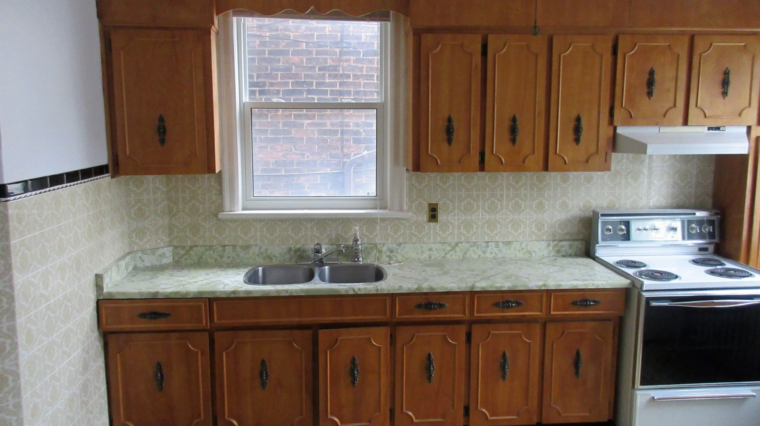 Kitchen with wooden cabinets, yellow patterned tile backsplash, a window above the sink, and an electric stove.