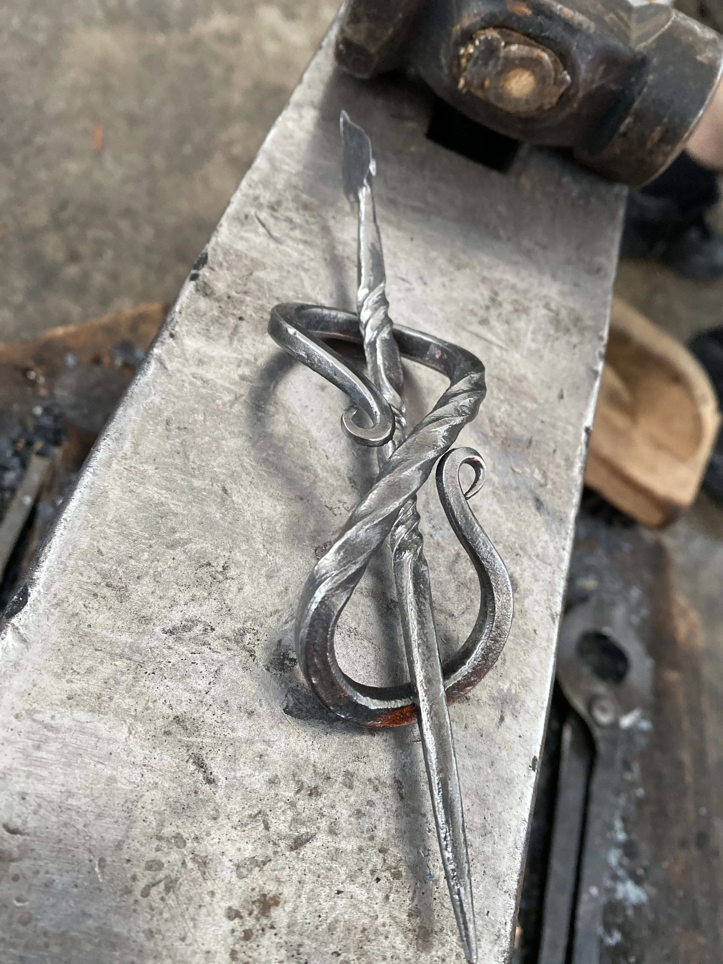 A metal forge hammer with a twisted handle and a pointed tip, resting on a workbench in a blacksmith workshop.