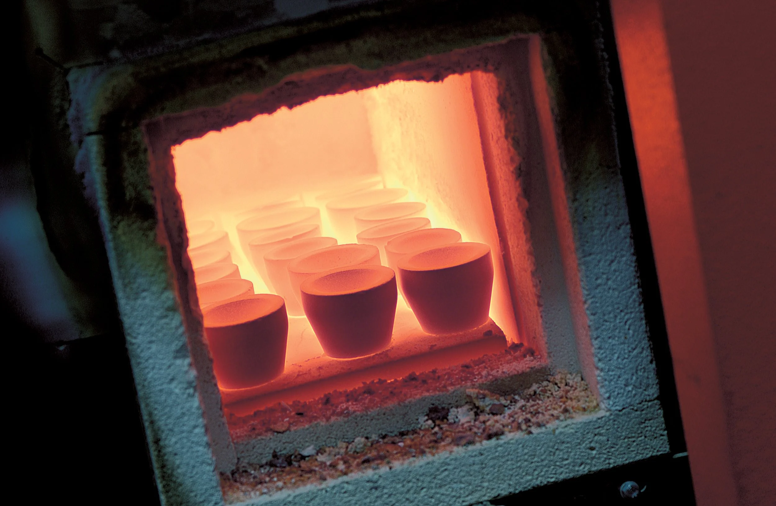 Ceramic cups inside a kiln with glowing orange heating elements.