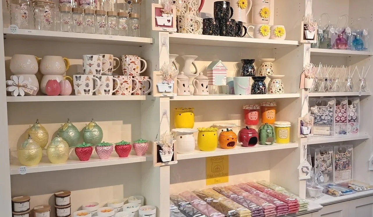 Shelves filled with various colorful ceramic mugs, soy wax container candles, wax melt burners and gift sets in a gift shop.