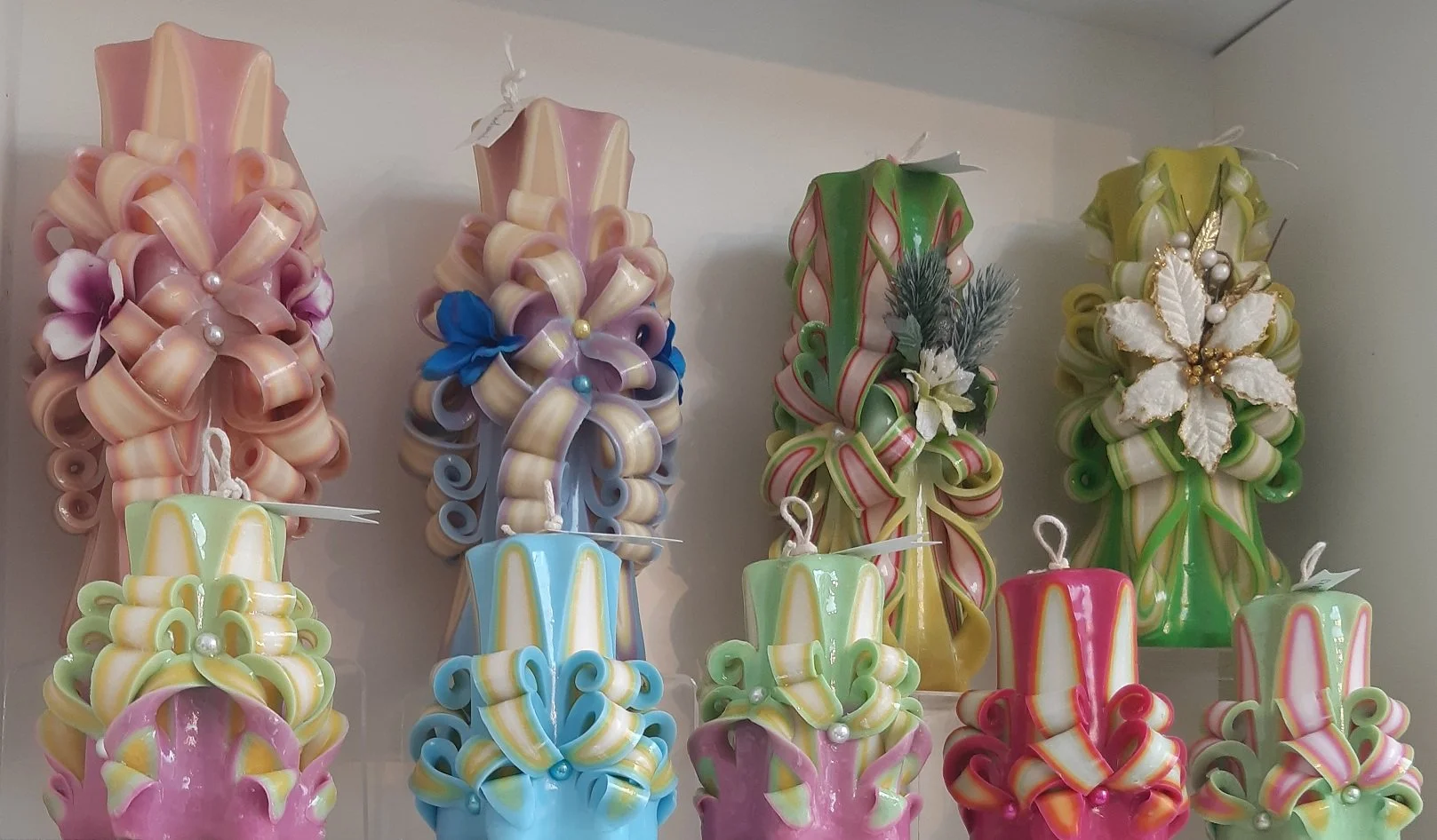 Decorative hand carved candles in pink, blue, green, yellow, red with bows and ribbons embellishments.