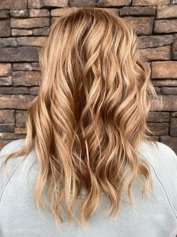 Rear view of long wavy hair featuring sun-kissed honey blonde balayage and soft hand-painted dimension.