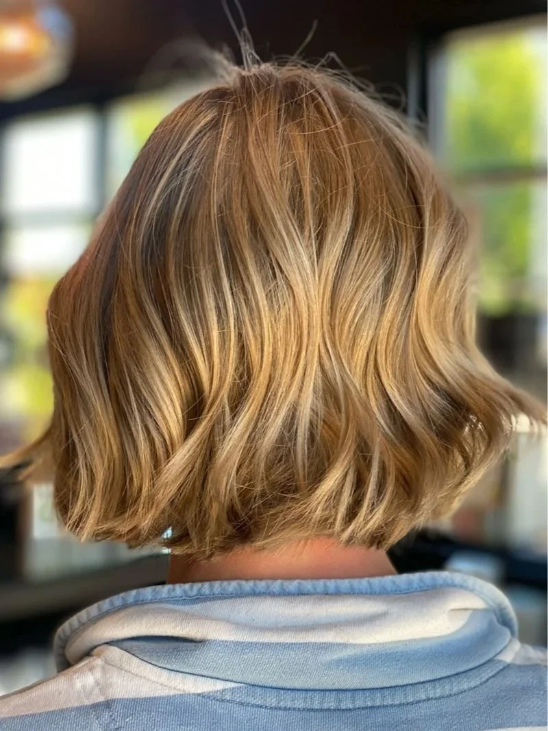 Rear view of short wavy hair featuring sun-kissed honey blonde balayage and soft hand-painted dimension.