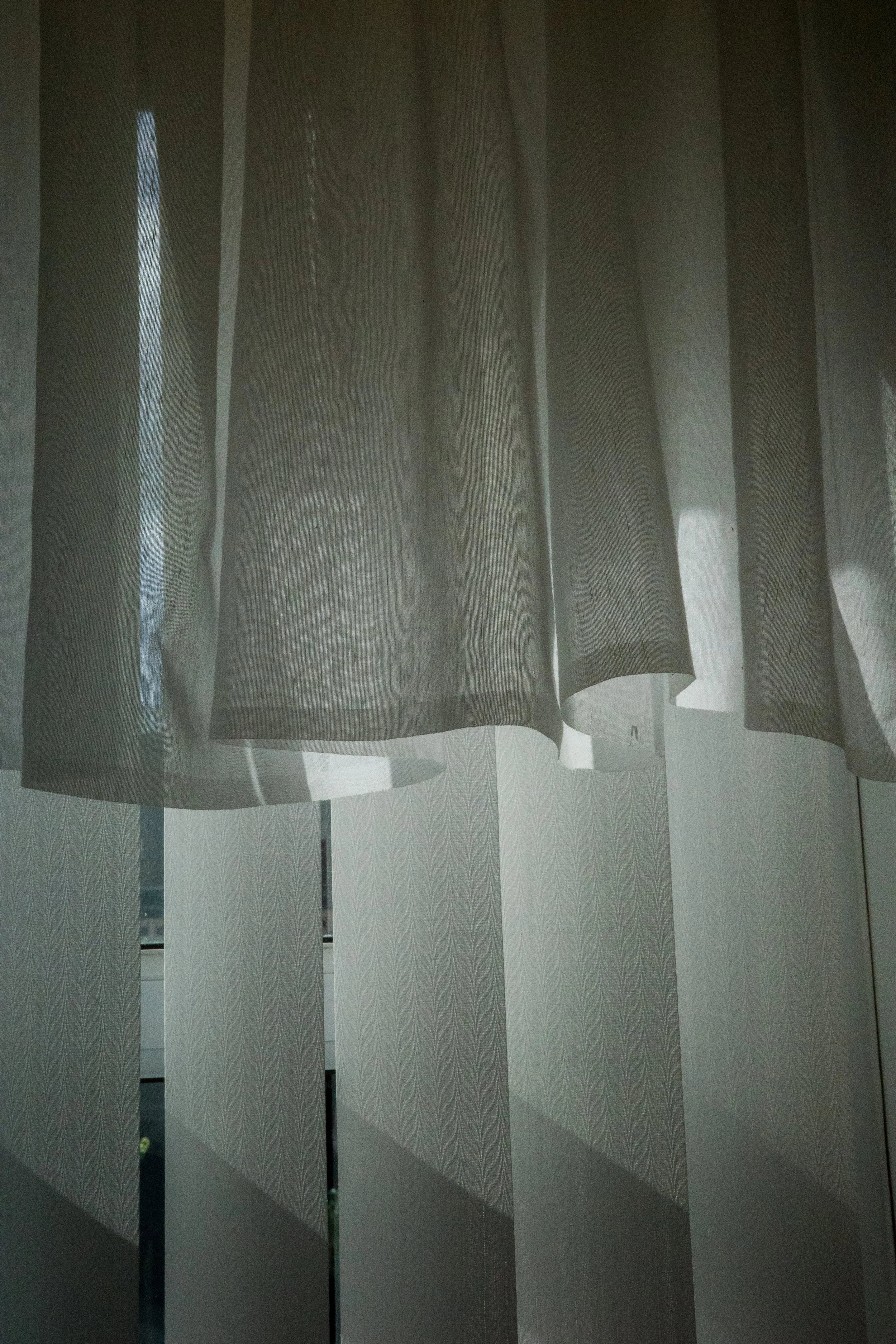 Light-colored sheer curtains hanging in front of a window, with light filtering through.