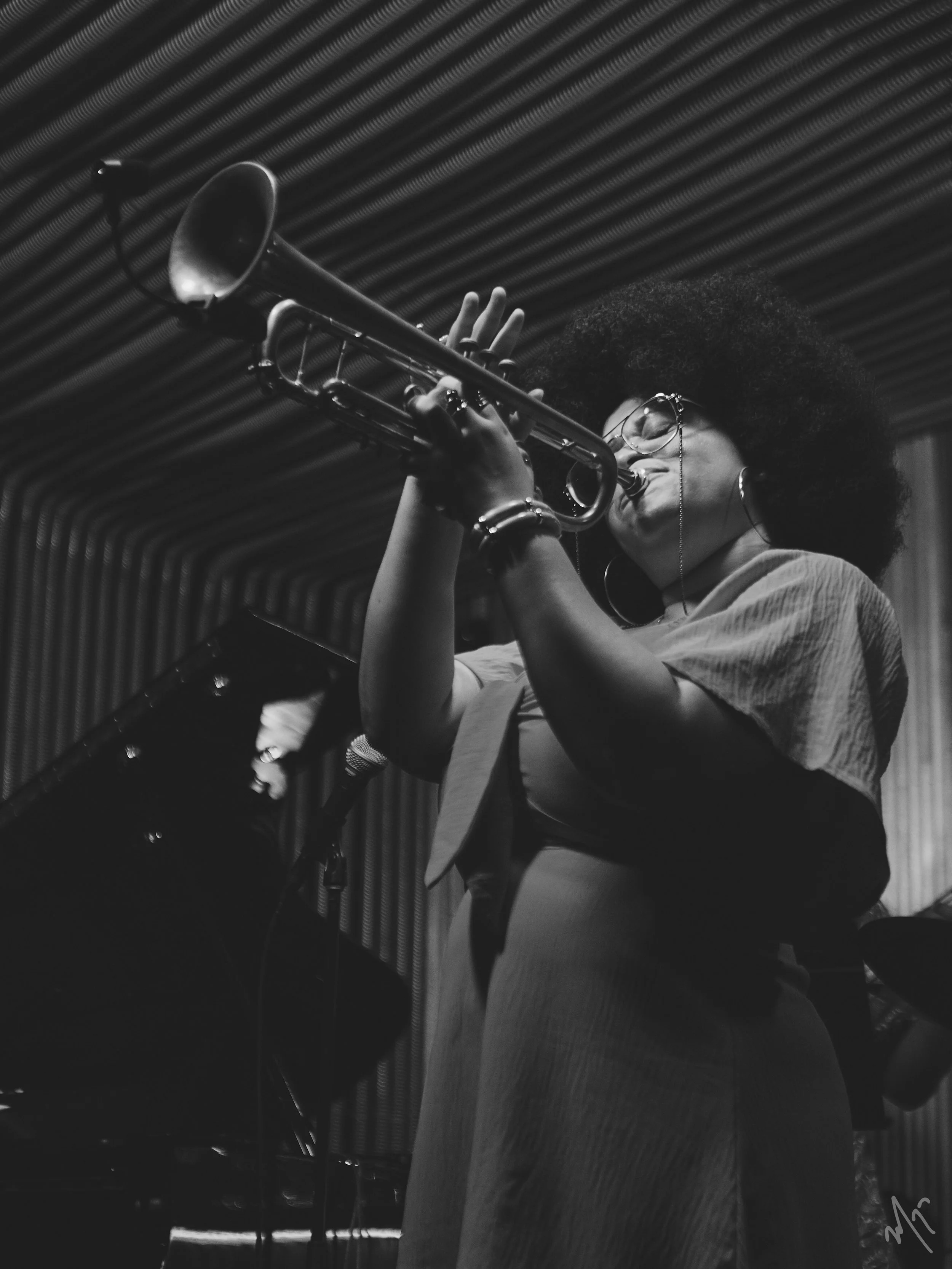 Tatiana Tate playing a trumpet in a music studio with a textured ceiling.