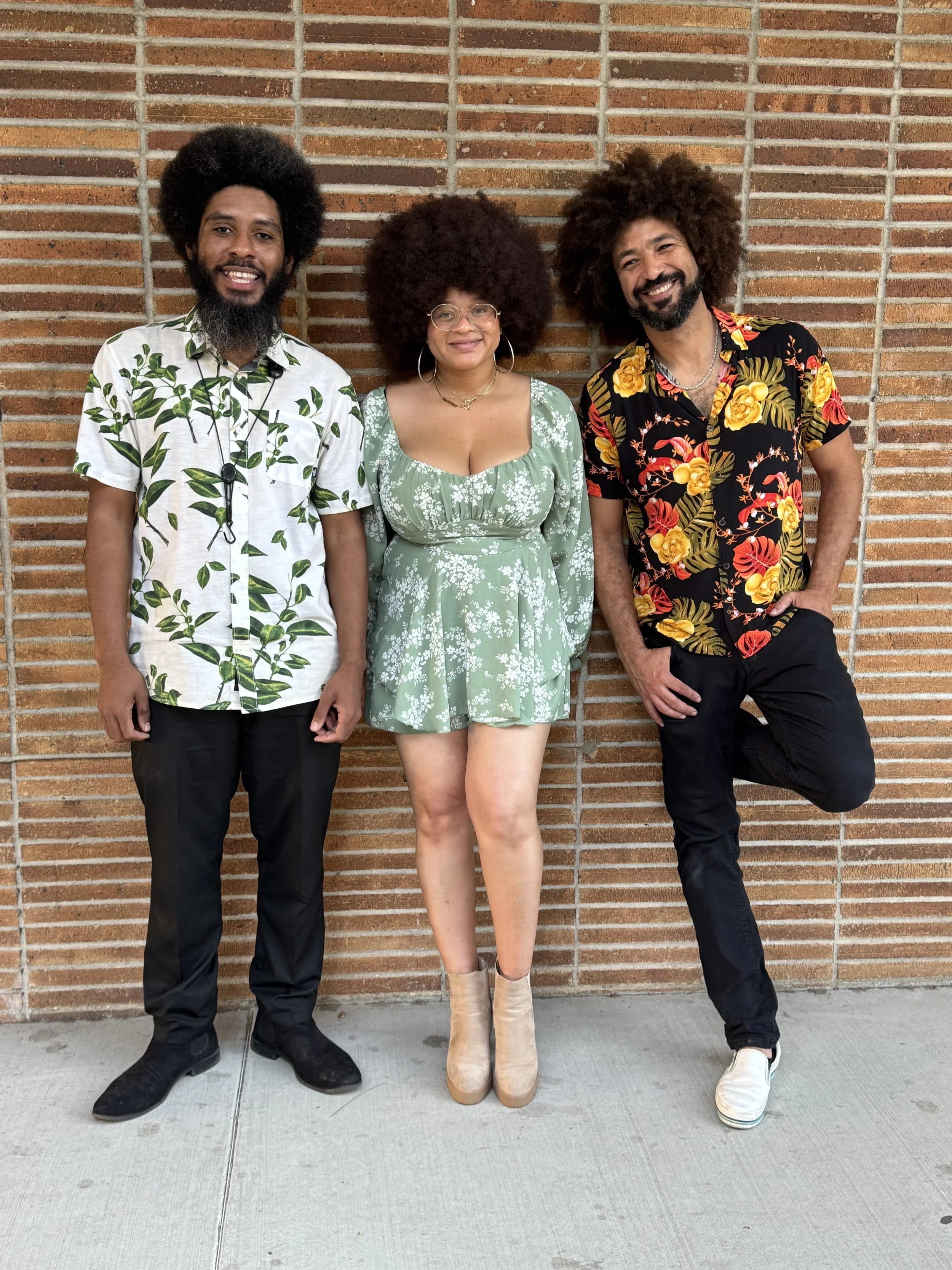 Tatiana Tate, the Melanin Horns, standing in front of a brick wall, smiling.