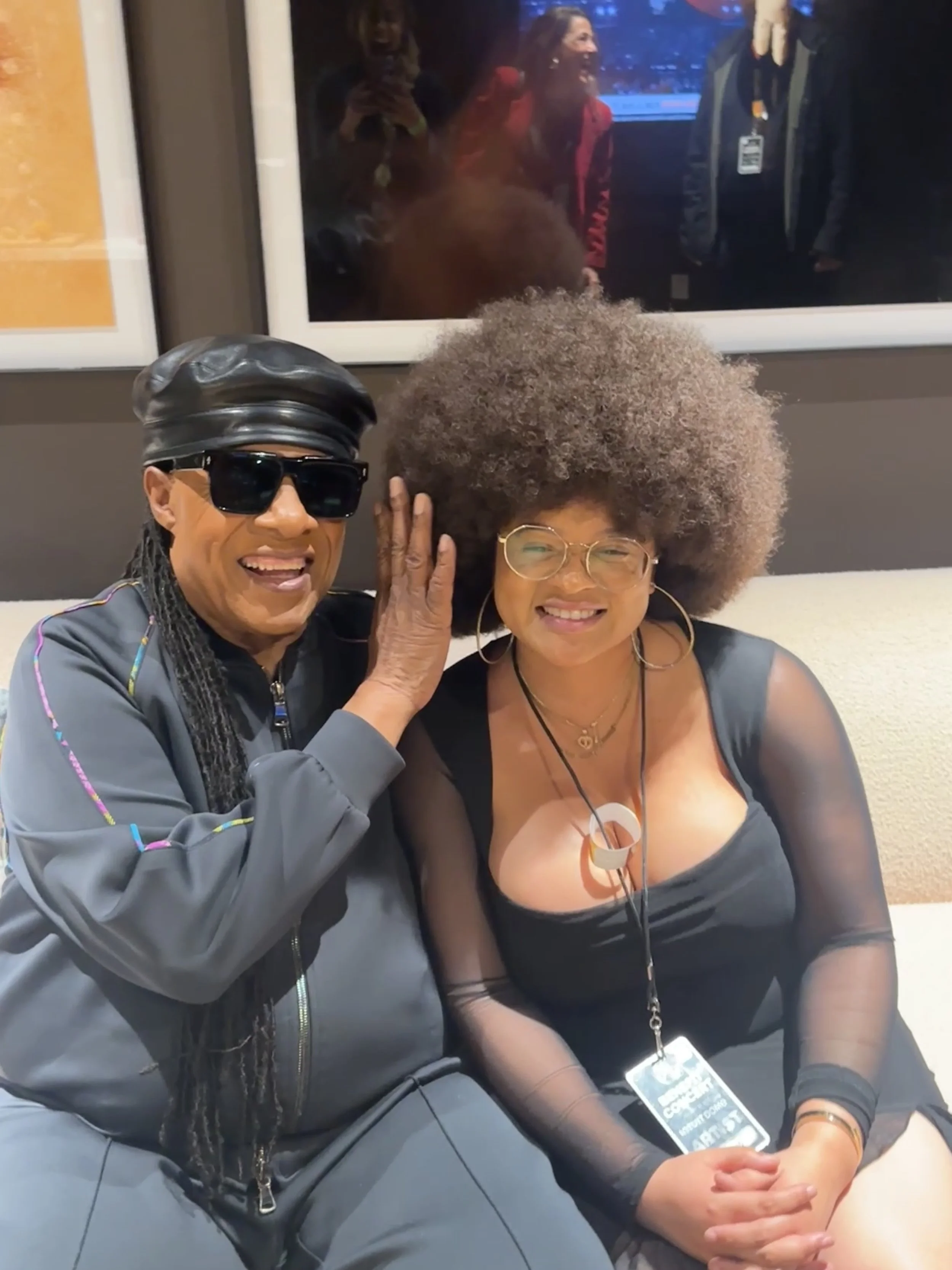 Tatiana Tate and Stevie Wonder sitting closely, smiling, with one touching the other's face gently. 
