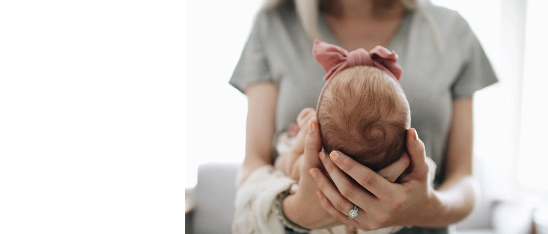 Person holding a baby's head in their hands, with the baby wearing a pink headband, indoors with natural light.