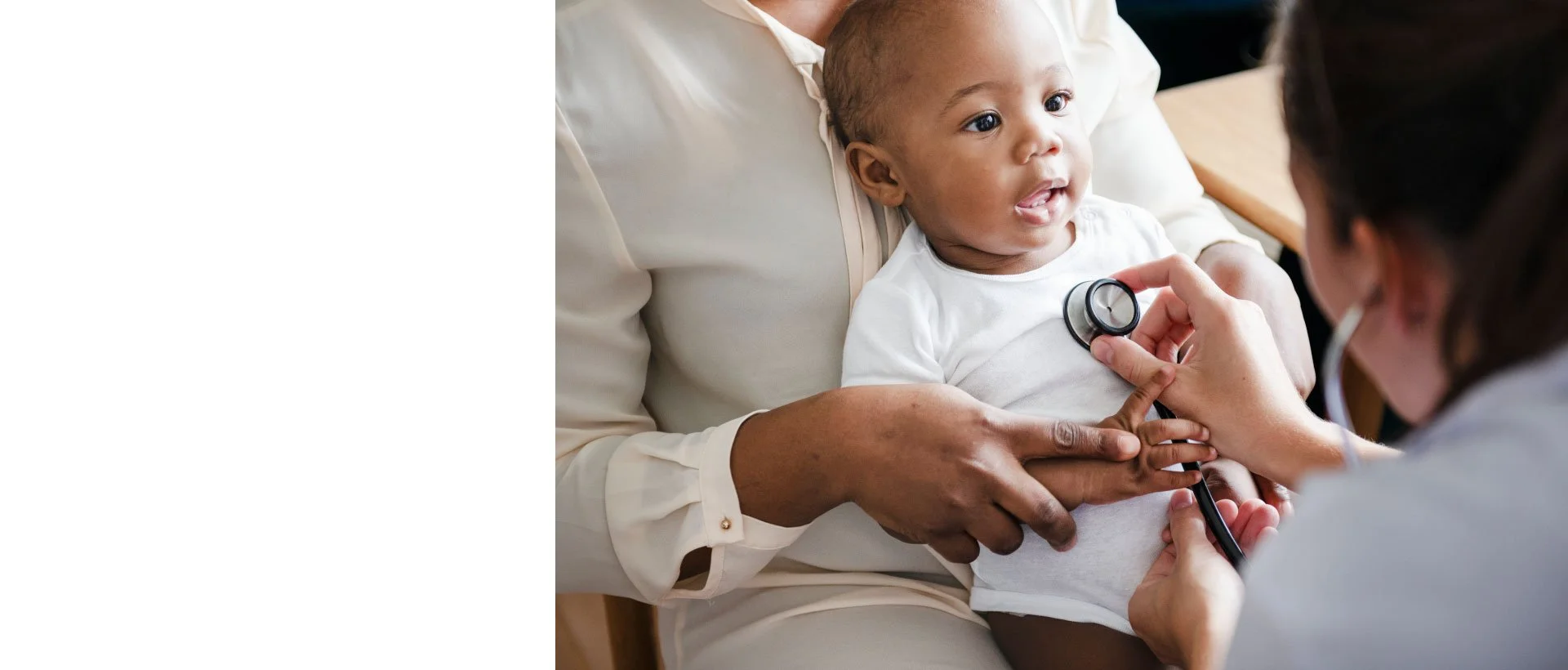 Pediatrician examining a young child's heart with a stethoscope as the caregiver holds the child.