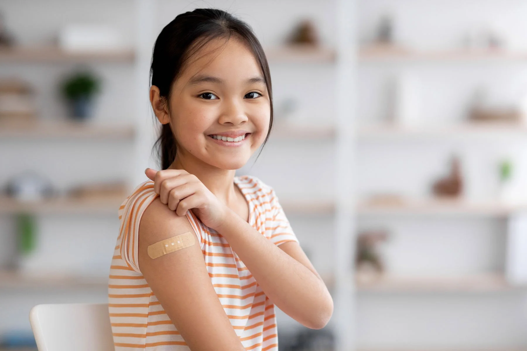 Young girl smiling and showing her upper arm with a bandage after receiving a vaccination.