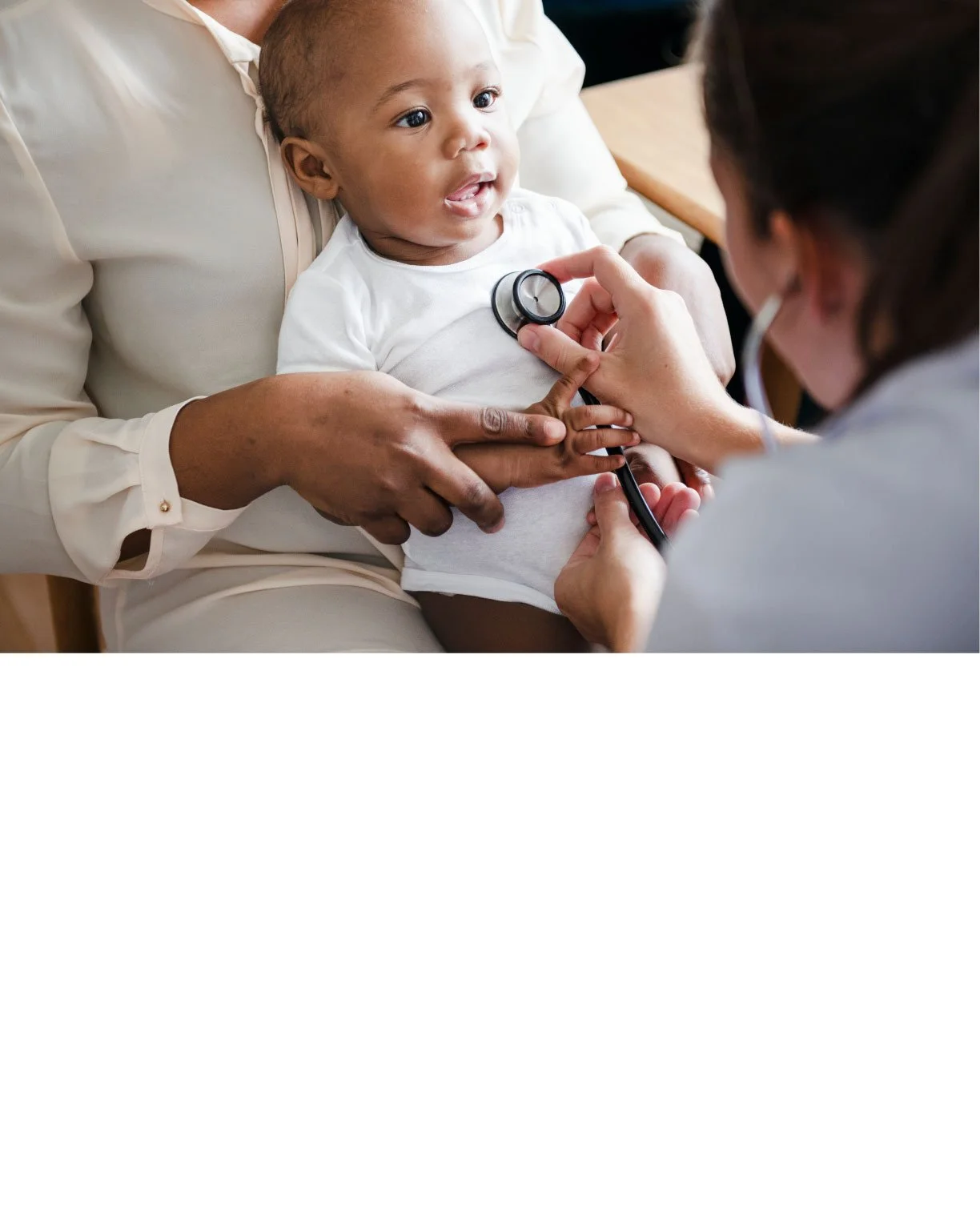 A doctor examining a young child with a stethoscope while the child is sitting on an adult's lap in an examination room.