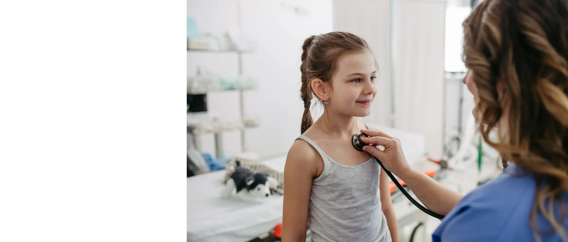 A young girl at a medical clinic having her heartbeat checked by a nurse using a stethoscope.
