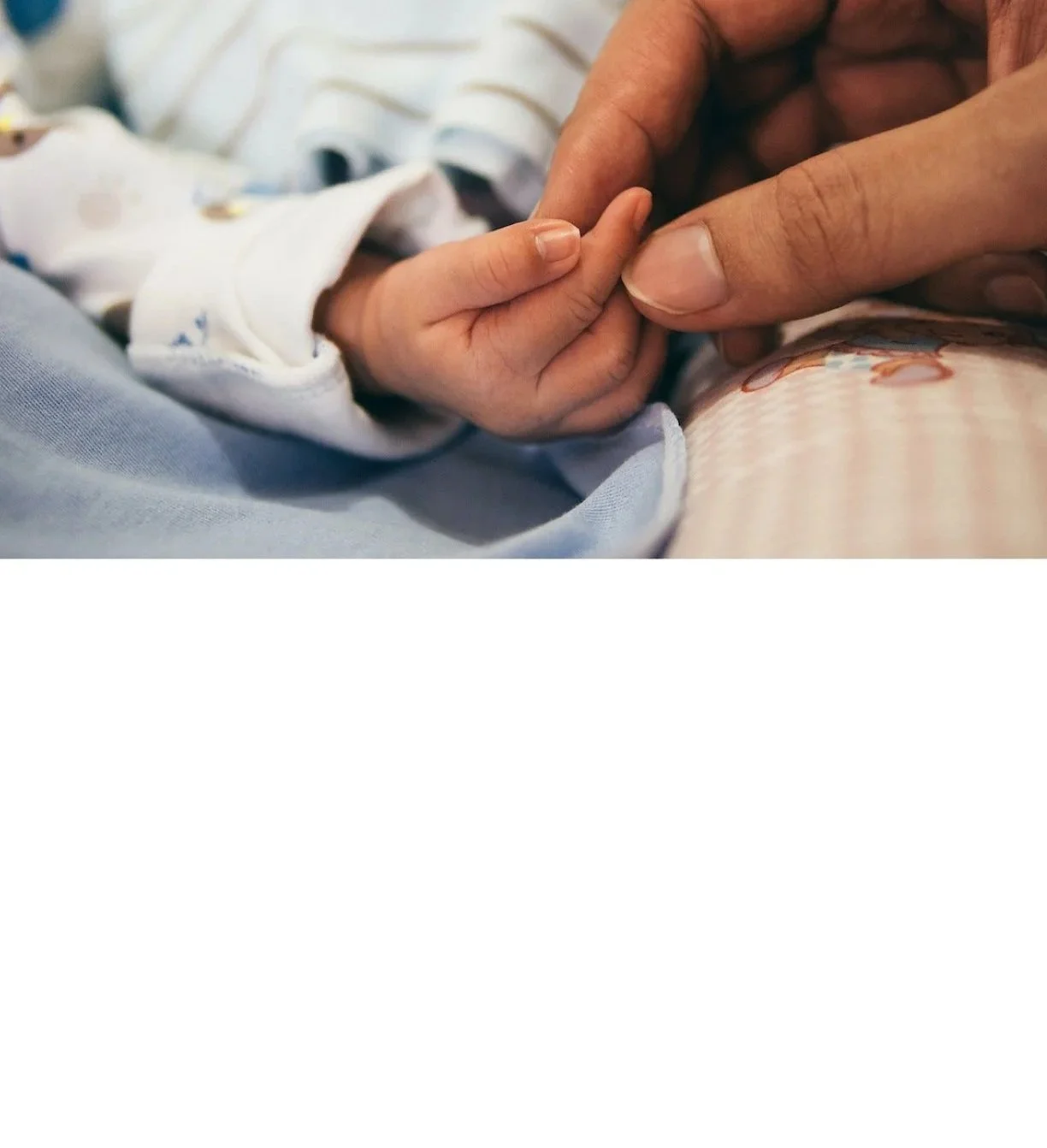 Close-up of an adult's hand holding the tiny hand of a baby, with the baby wearing a white long-sleeve outfit, emphasizing tenderness and connection.