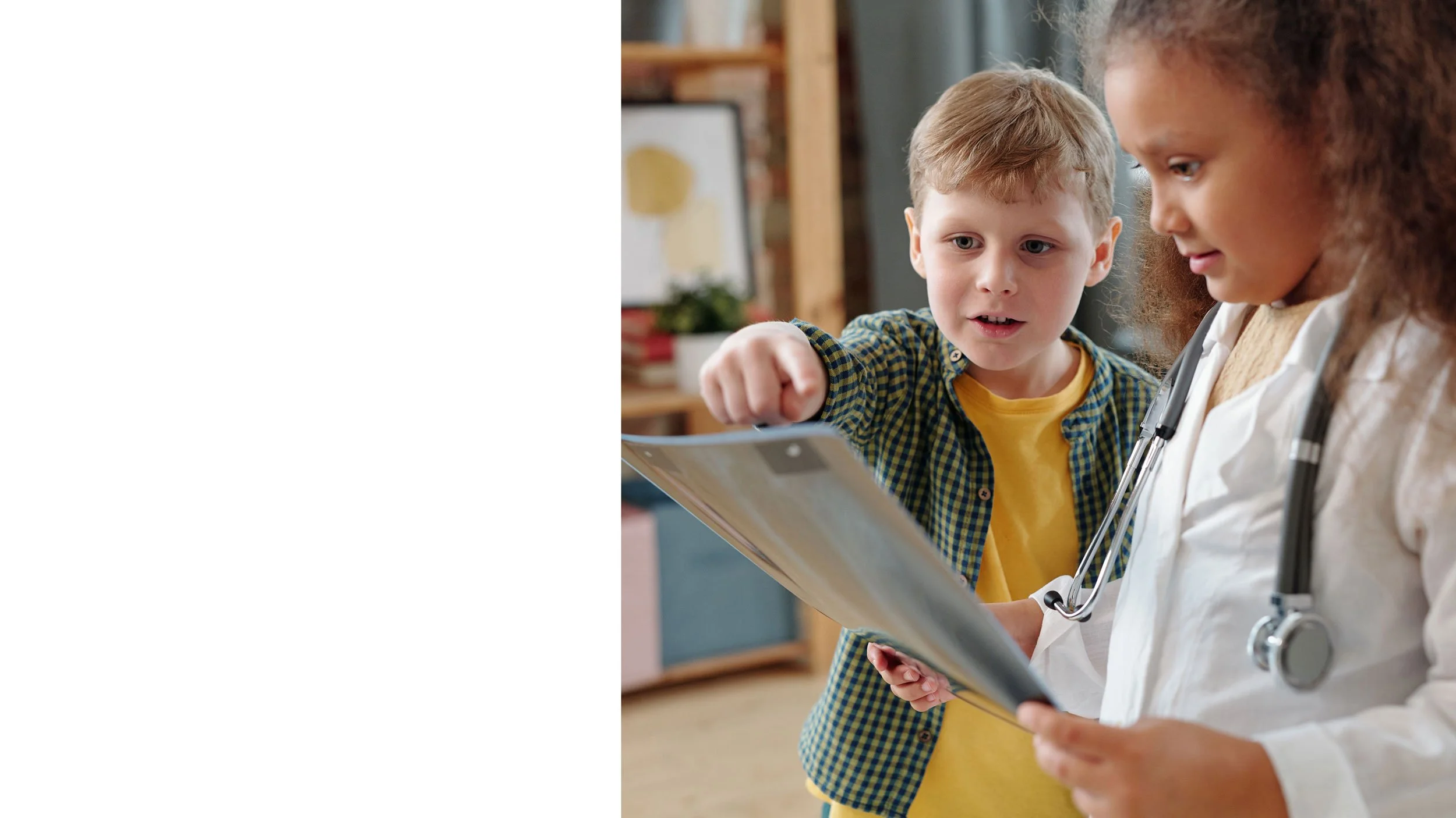 A young girl with light brown, wavy hair lying on a bed next to a sleeping infant wrapped in a white blanket. The girl is smiling slightly and wearing a white shirt with black buttons.
