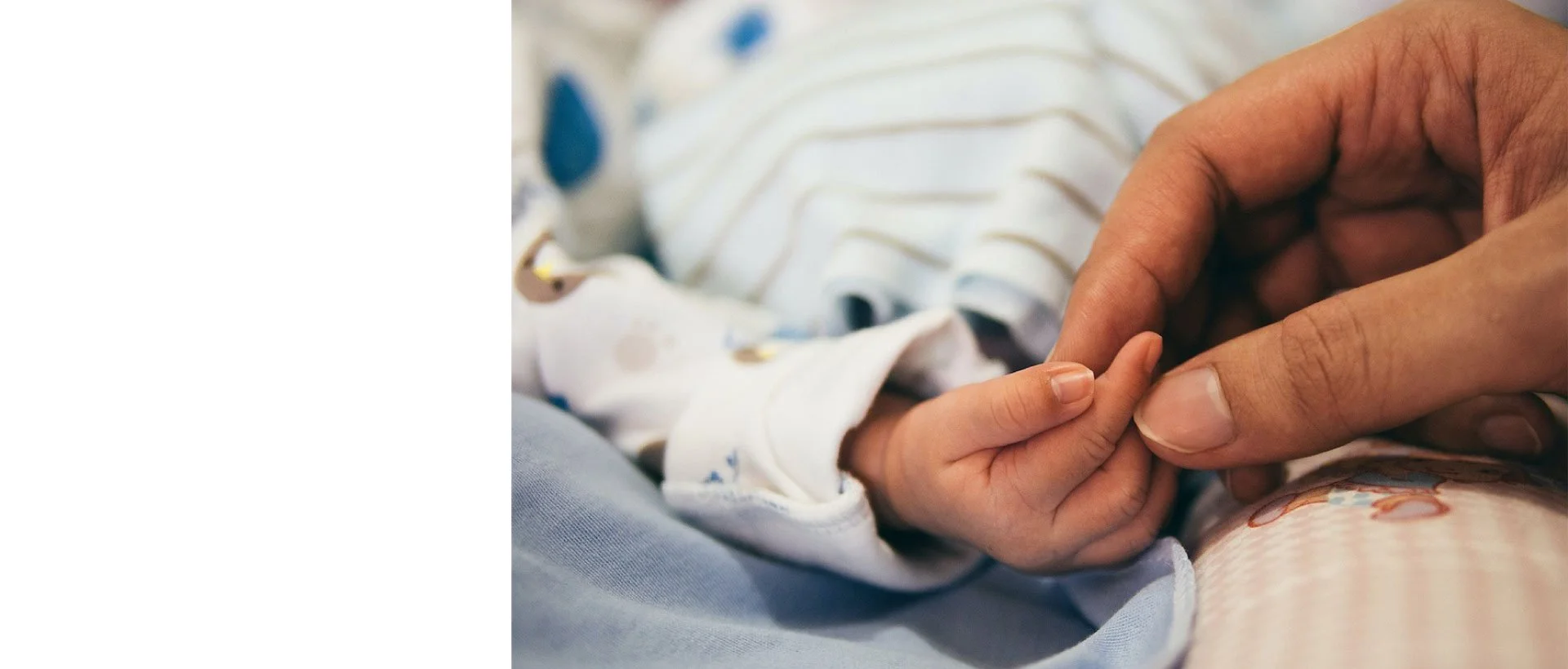 Close-up of an adult holding a baby's tiny hand, with the baby wearing a striped onesie.