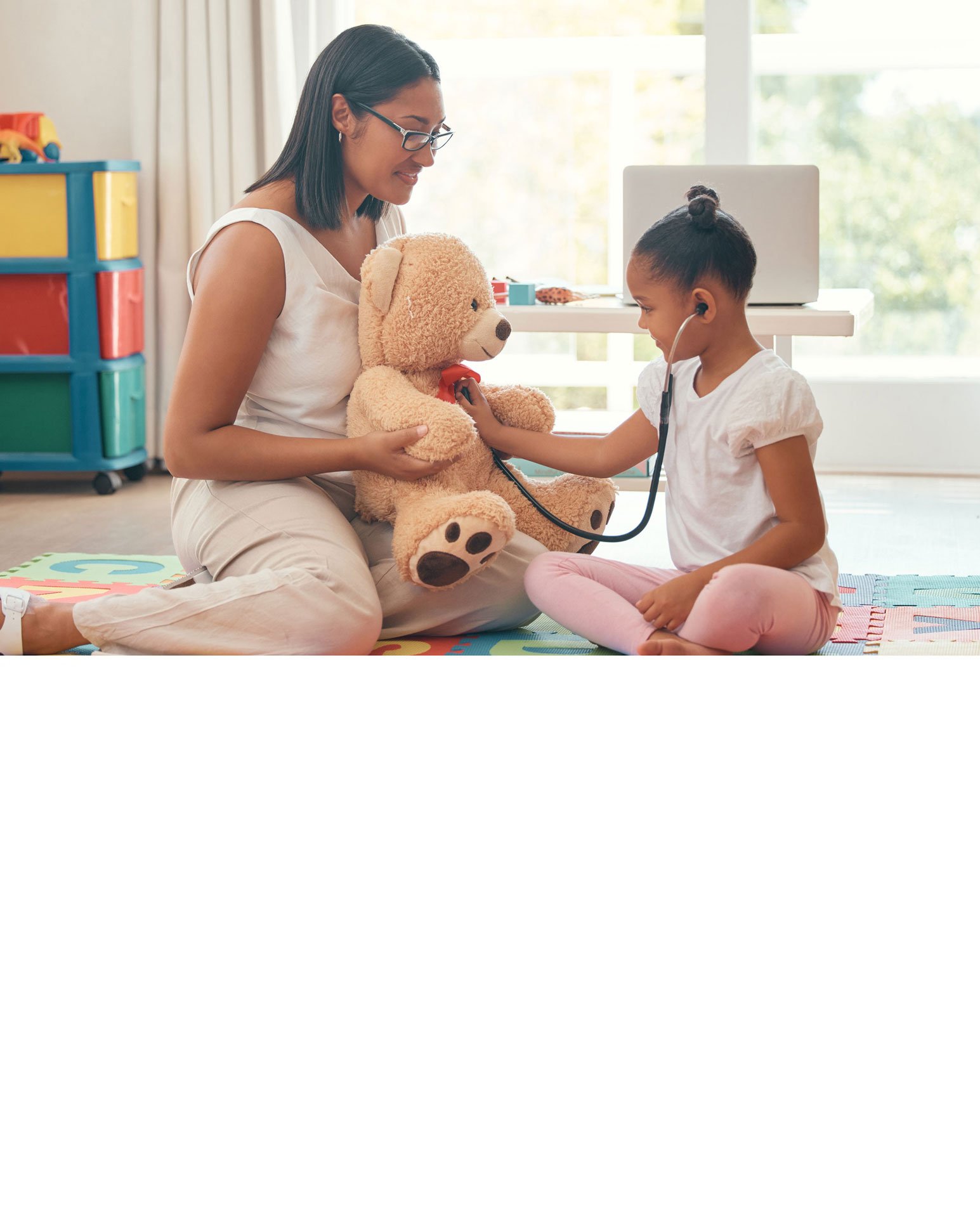 A woman with dark hair and a striped sweater smiling while holding a young child with short hair and a white hoodie, both looking at something in front of them.