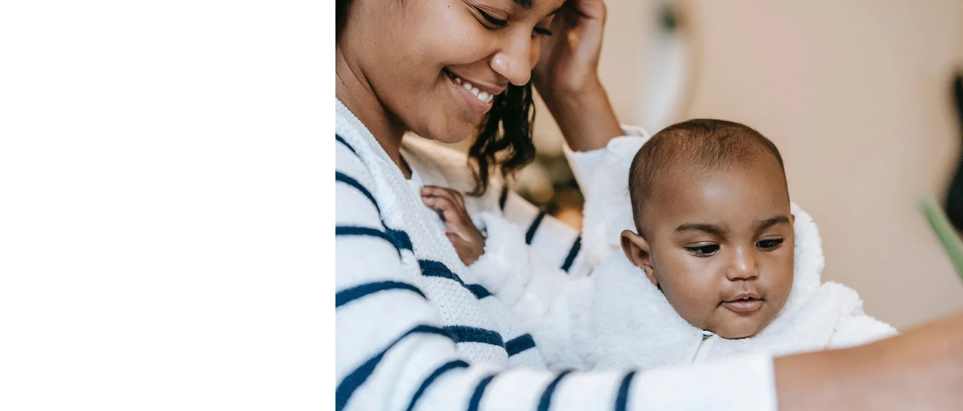 A woman smiling down at a young boy who is looking at something off-camera, both wearing white tops, in a close-up indoor setting.