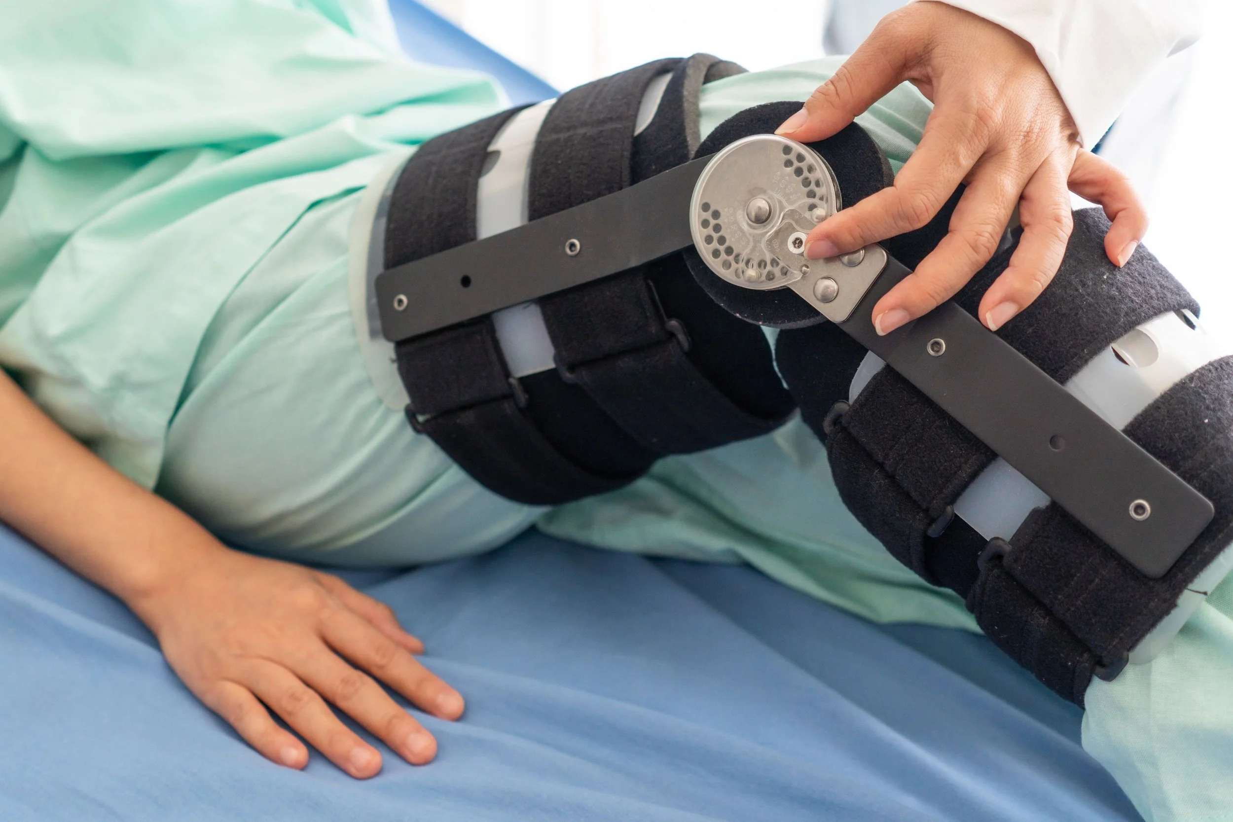 Person lying on a blue hospital bed with a leg brace and external fixator device on their leg, being adjusted by a healthcare professional.