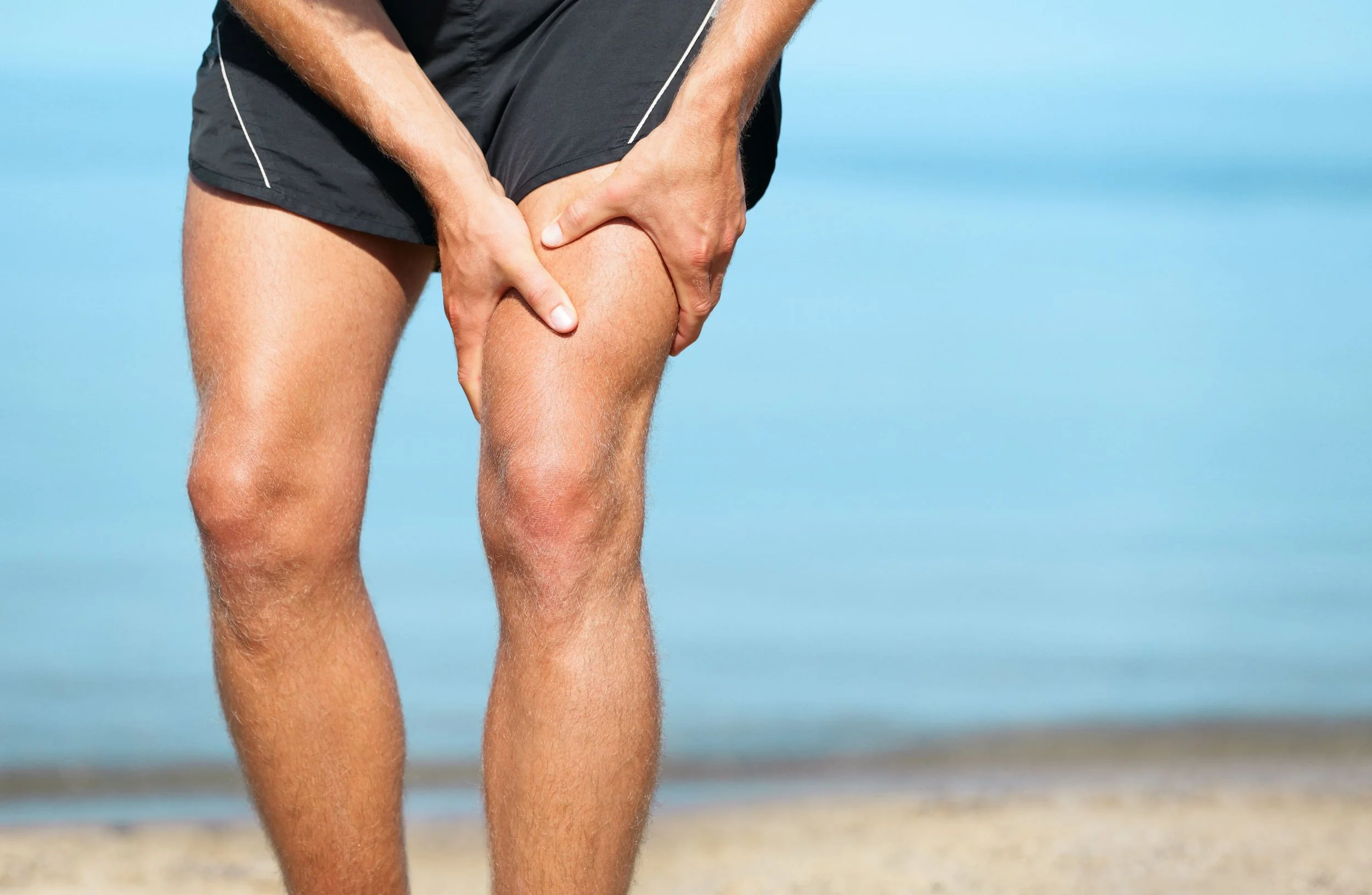 Man wearing black shorts holding his knee on a beach.