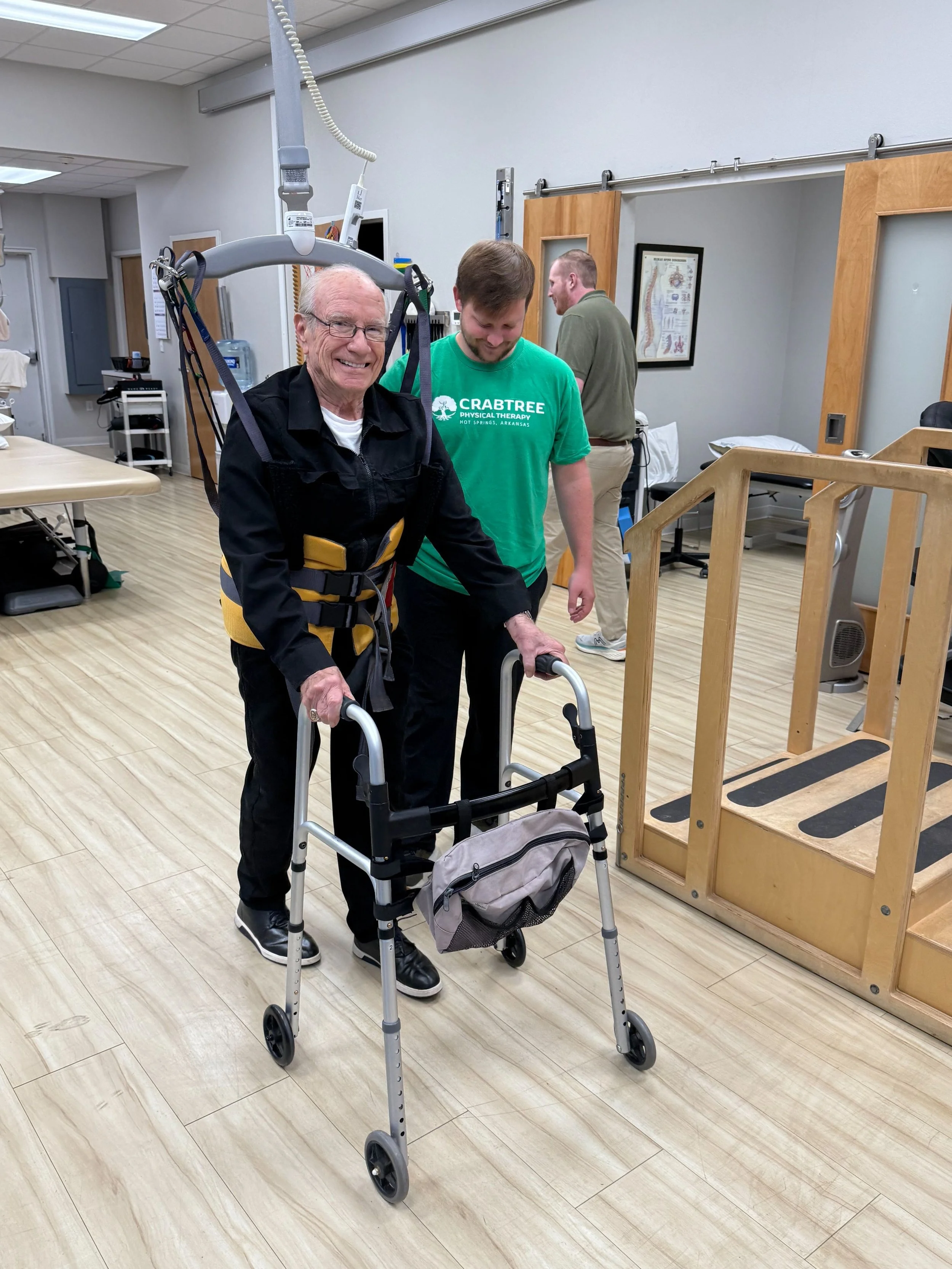 An elderly man using a walker in a physical therapy room with assistance from a Crabtree Physical Therapy therapist.