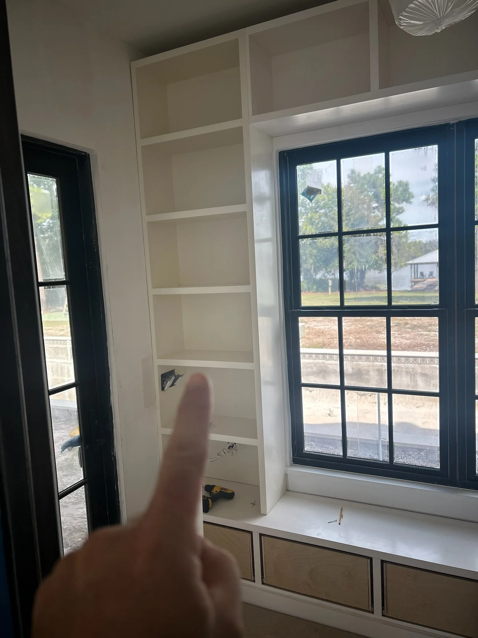 Empty built-in bookshelf next to large window in a room under construction.
