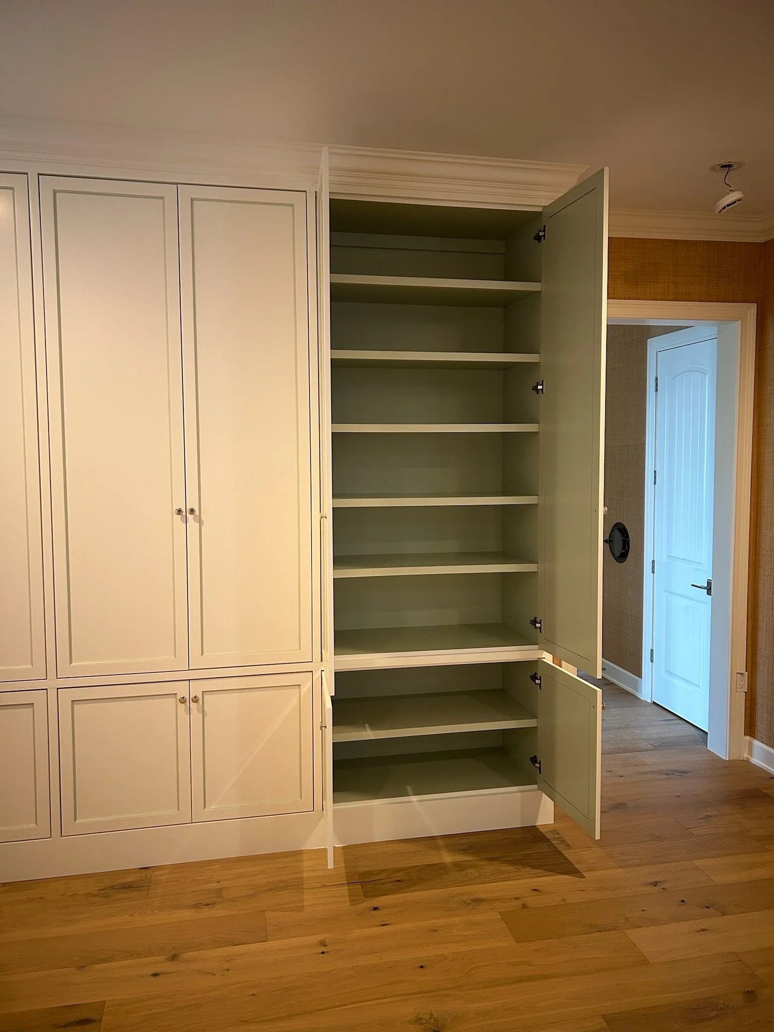 Empty green and white built-in cabinets with open doors, standing against a wall in a room with wooden flooring.