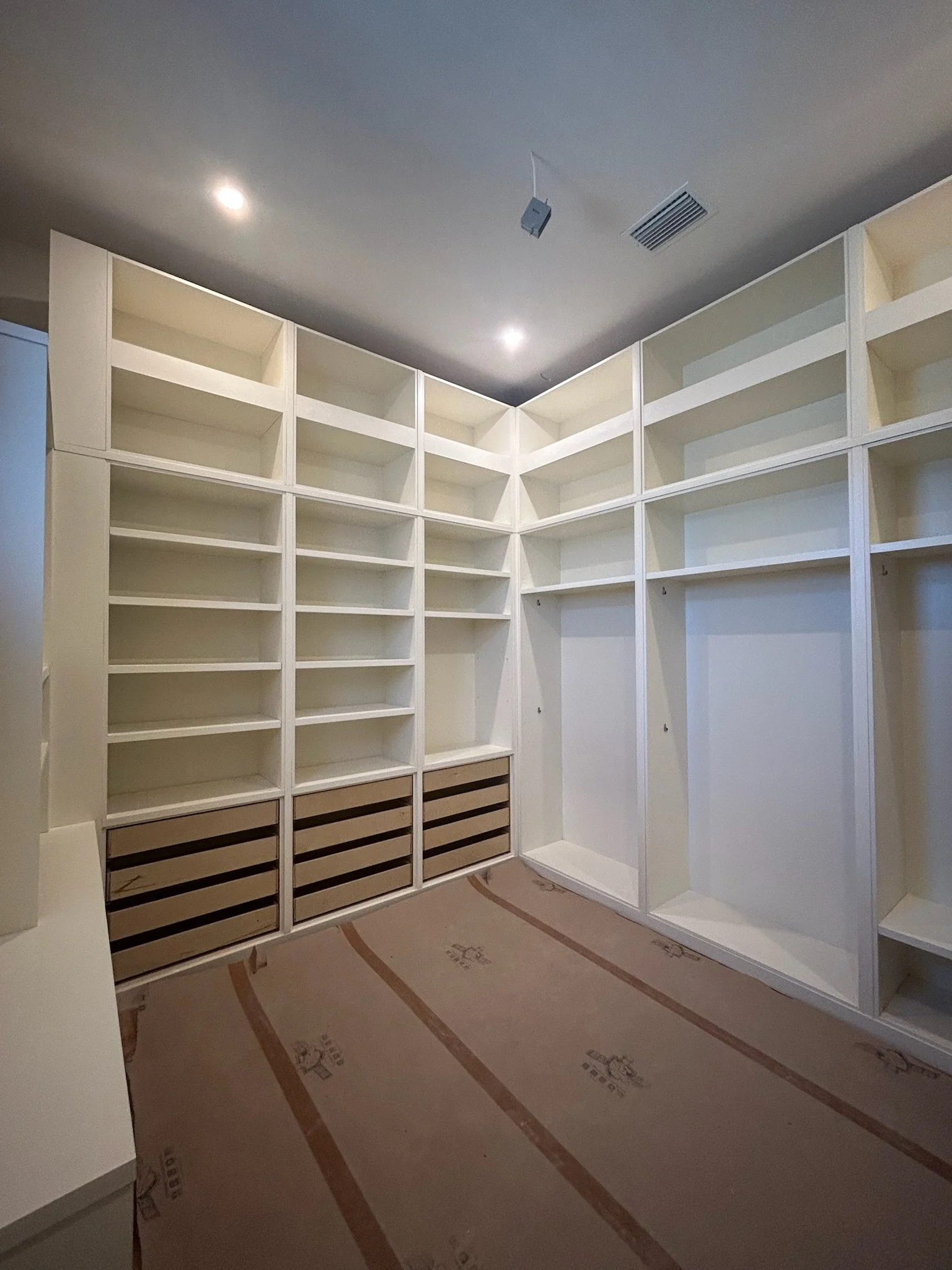 Empty white built-in shelves and closet space in a room under construction with a plastic protective covering on the floor.