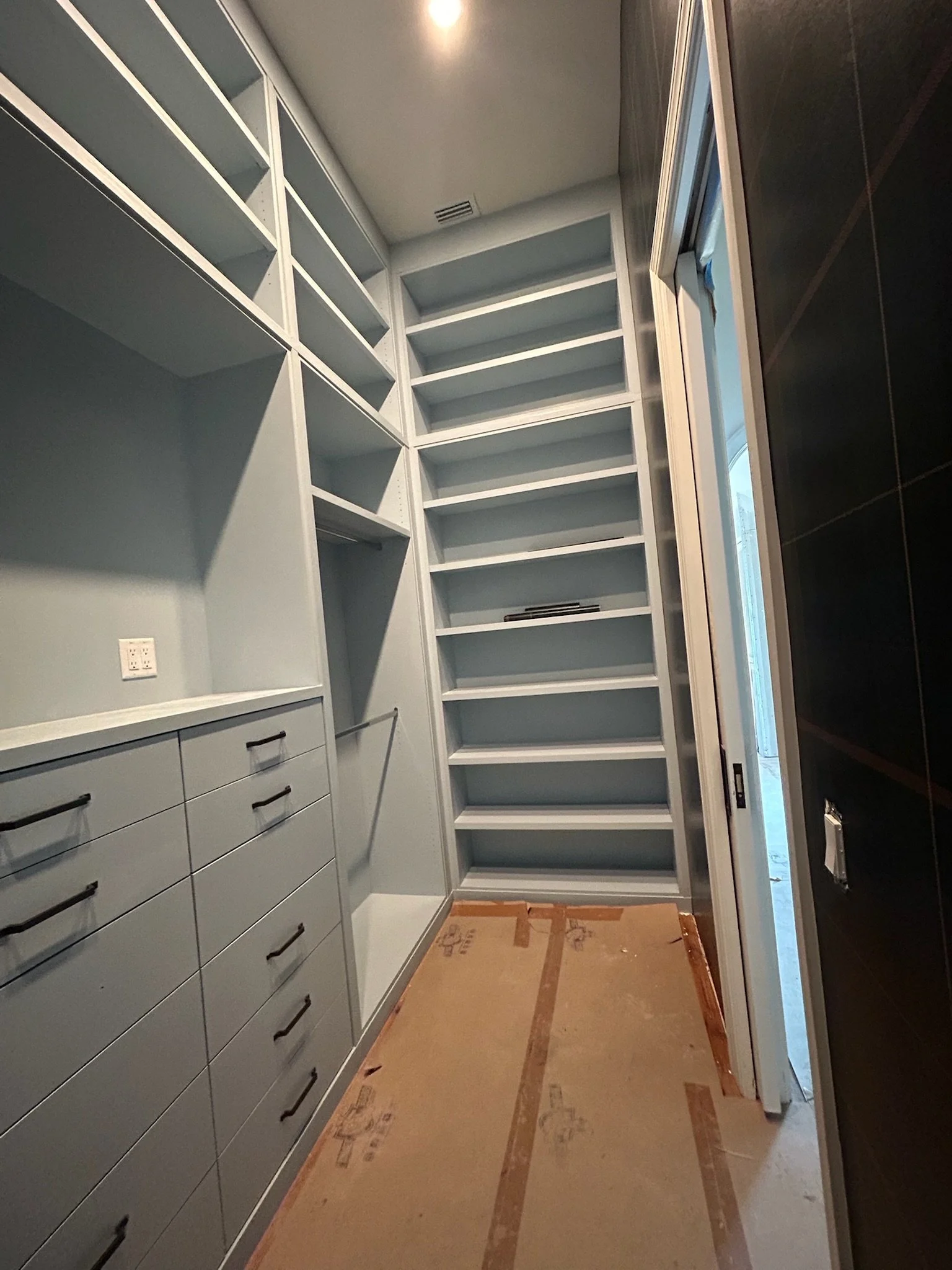 Empty walk-in custom closet with built-in shelves, drawers, and a sliding door.