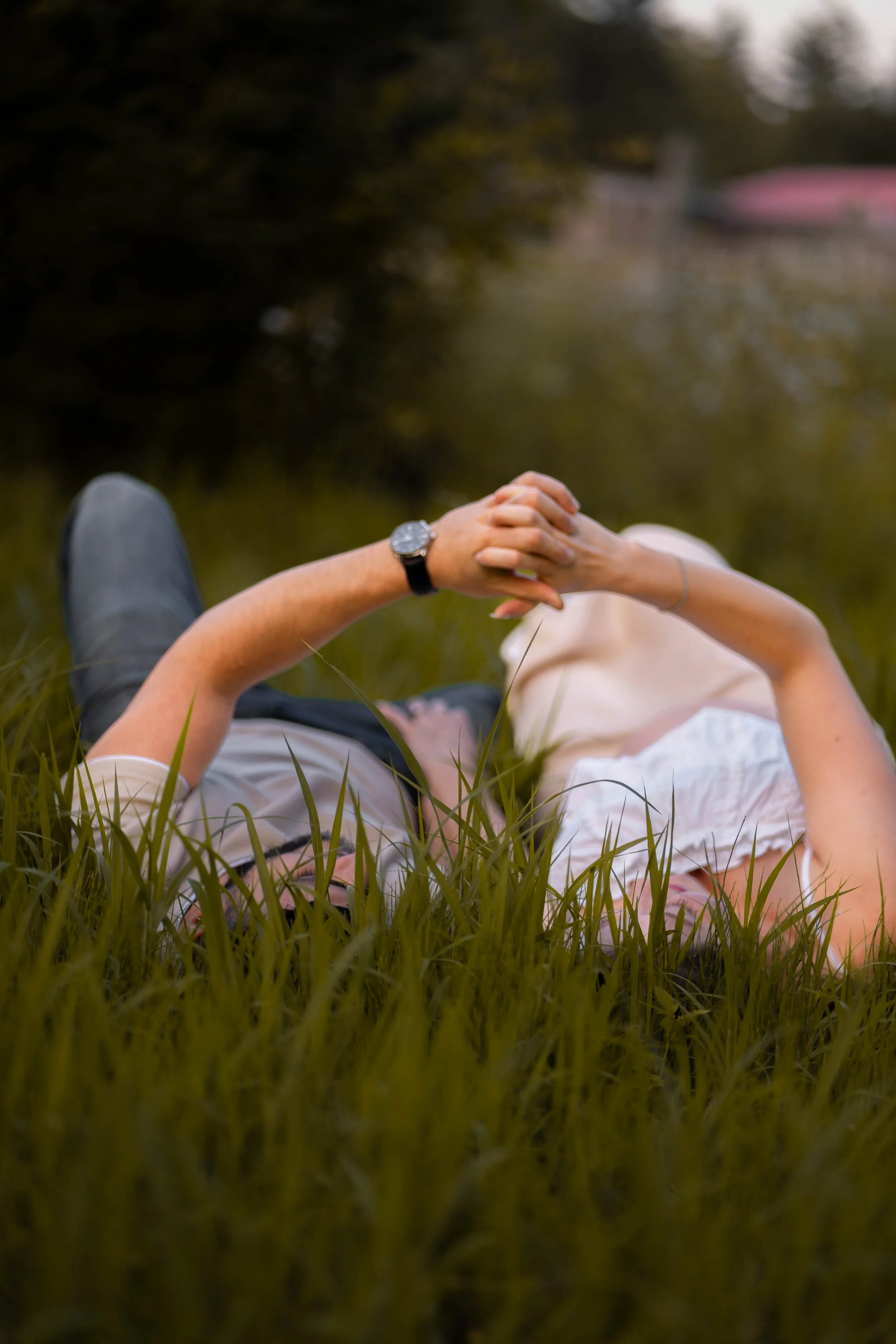 Person lying on grass with hands clasped, wearing glasses, a watch, a white shirt, and beige shorts, relaxing outdoors.
