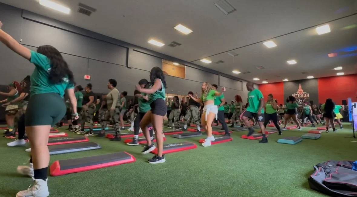 Group of people participating in a fitness class on an indoor turf field, using small step platforms for exercise.