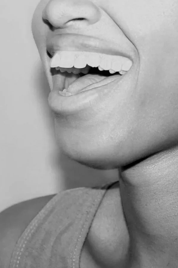 Close-up of a smiling person's face, showing their teeth and tongue, in black and white.