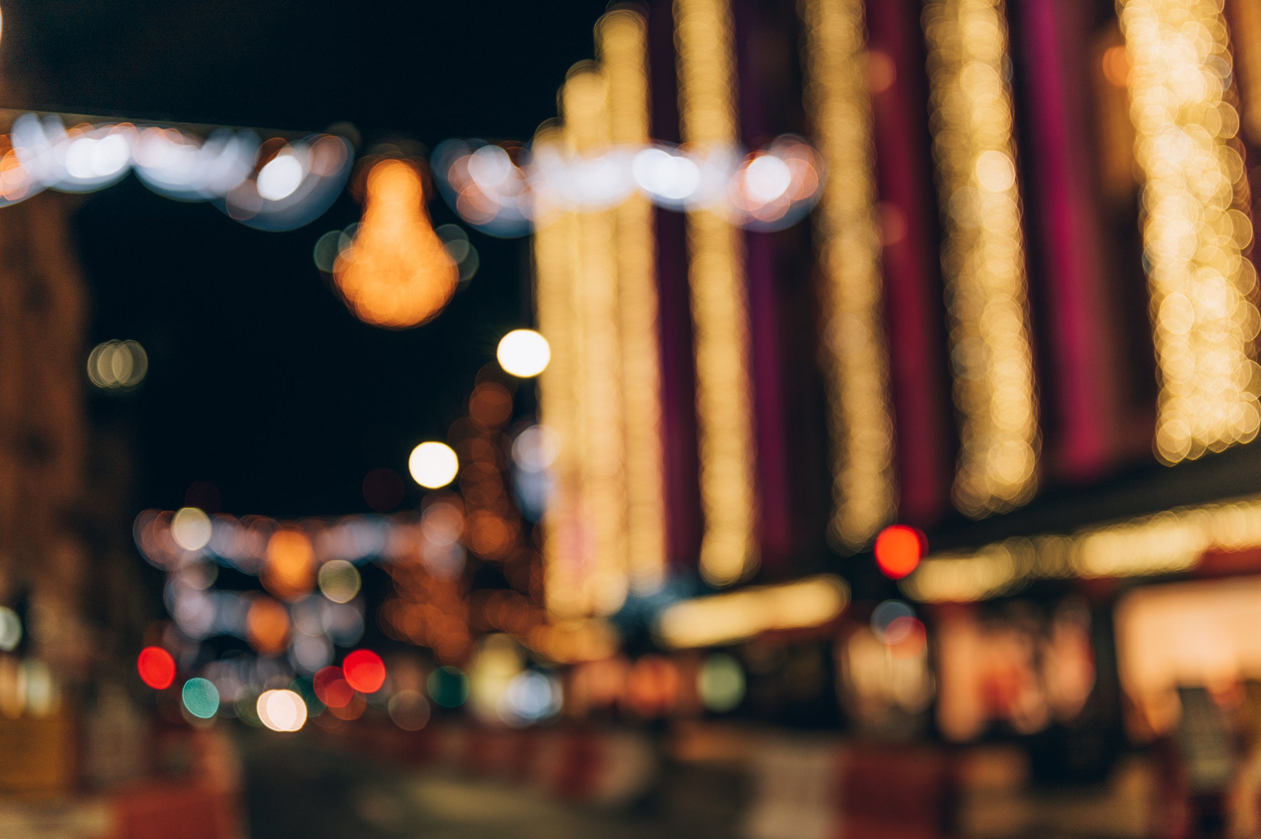 Blurred view of city street at night with colorful string lights and illuminated buildings.