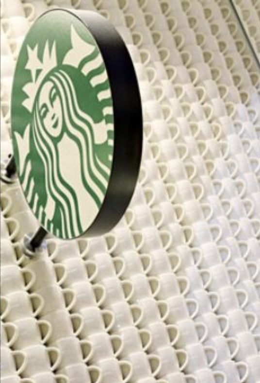 Starbucks logo sign mounted on a wall with a pattern of small white coffee mugs.