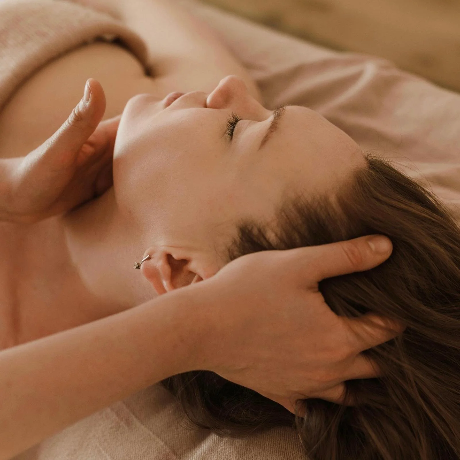 Eine Frau liegt auf einer Massageliege, sie erhält eine Behandlung aus Cranio-sacral-Therapie, Reiki und polyvagaler Regulation. Dabei wird ihr Kopf und ihre Schulter sanft berührt, sie ist tief entspannt