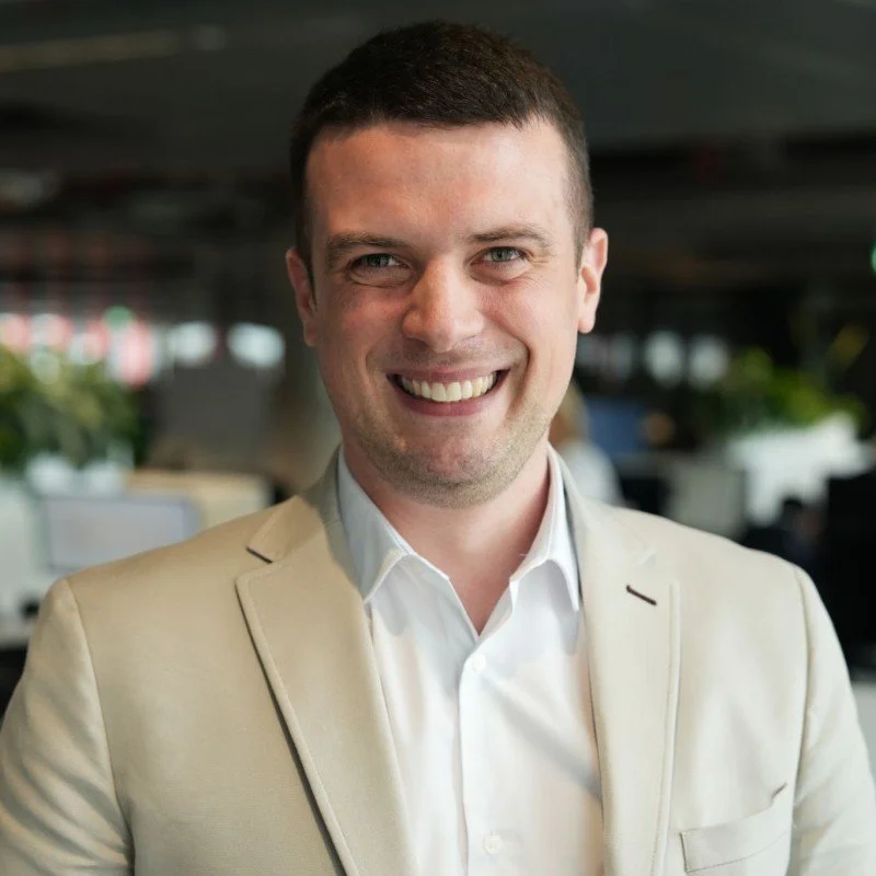 A smiling man in a light-colored blazer and white shirt in an indoor setting.