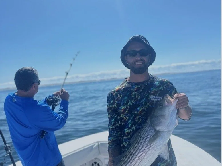Scenic view of a lake surrounded by green hills and mountains under a cloudy sky.