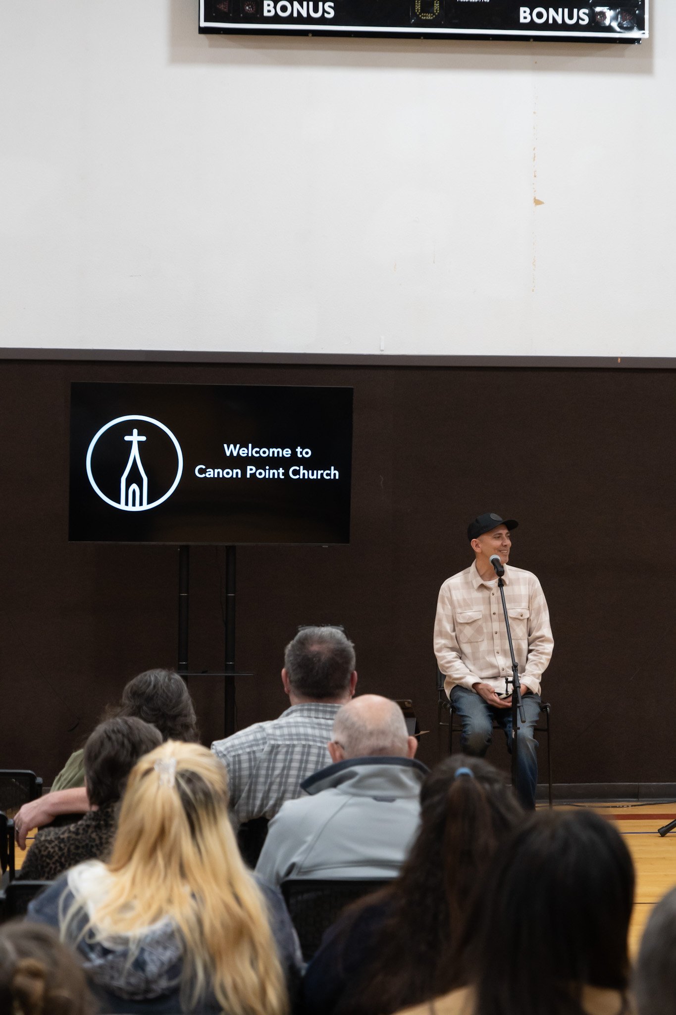 A man speaking on a microphone at Canon Point Church with an audience seated in front of him.