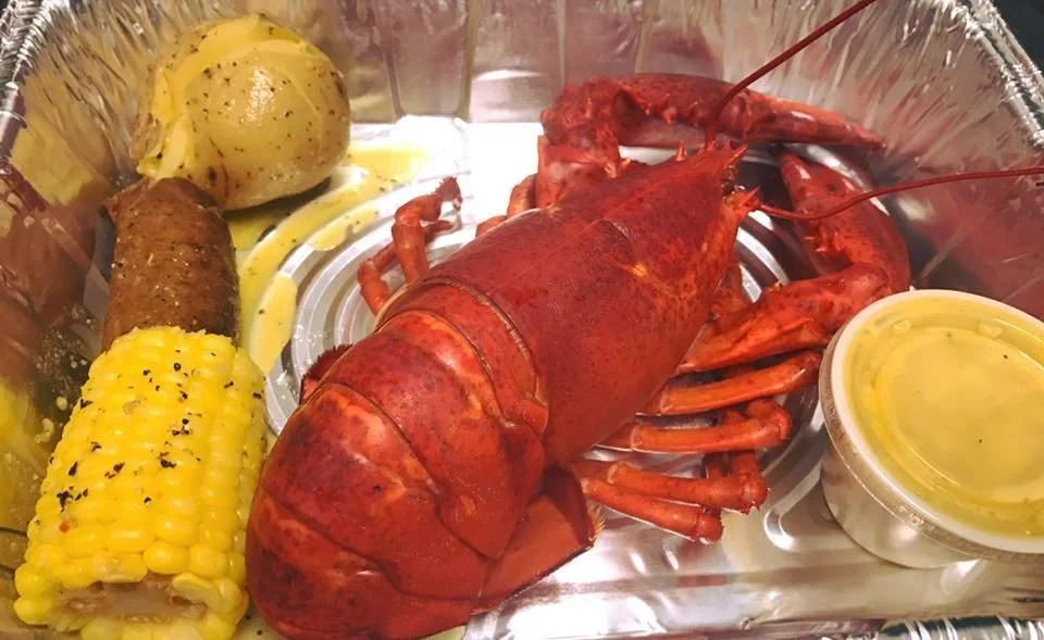 Whole lobster with corn, sausage, and potato in a takeout seafood combo tray