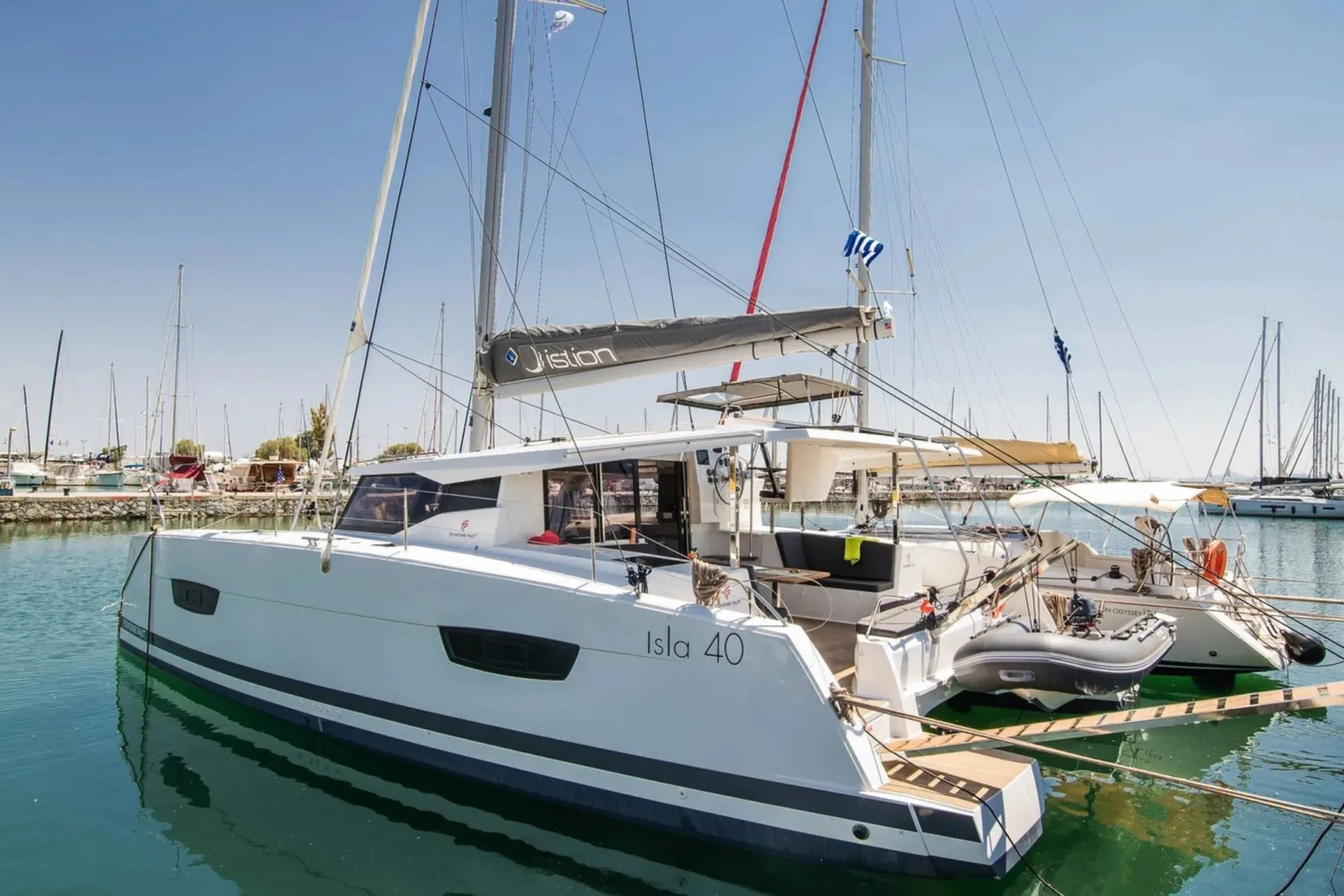 A white modern sailing yacht with the name 'Isla 40' docked at a marina, surrounded by other sailboats, under a clear blue sky.