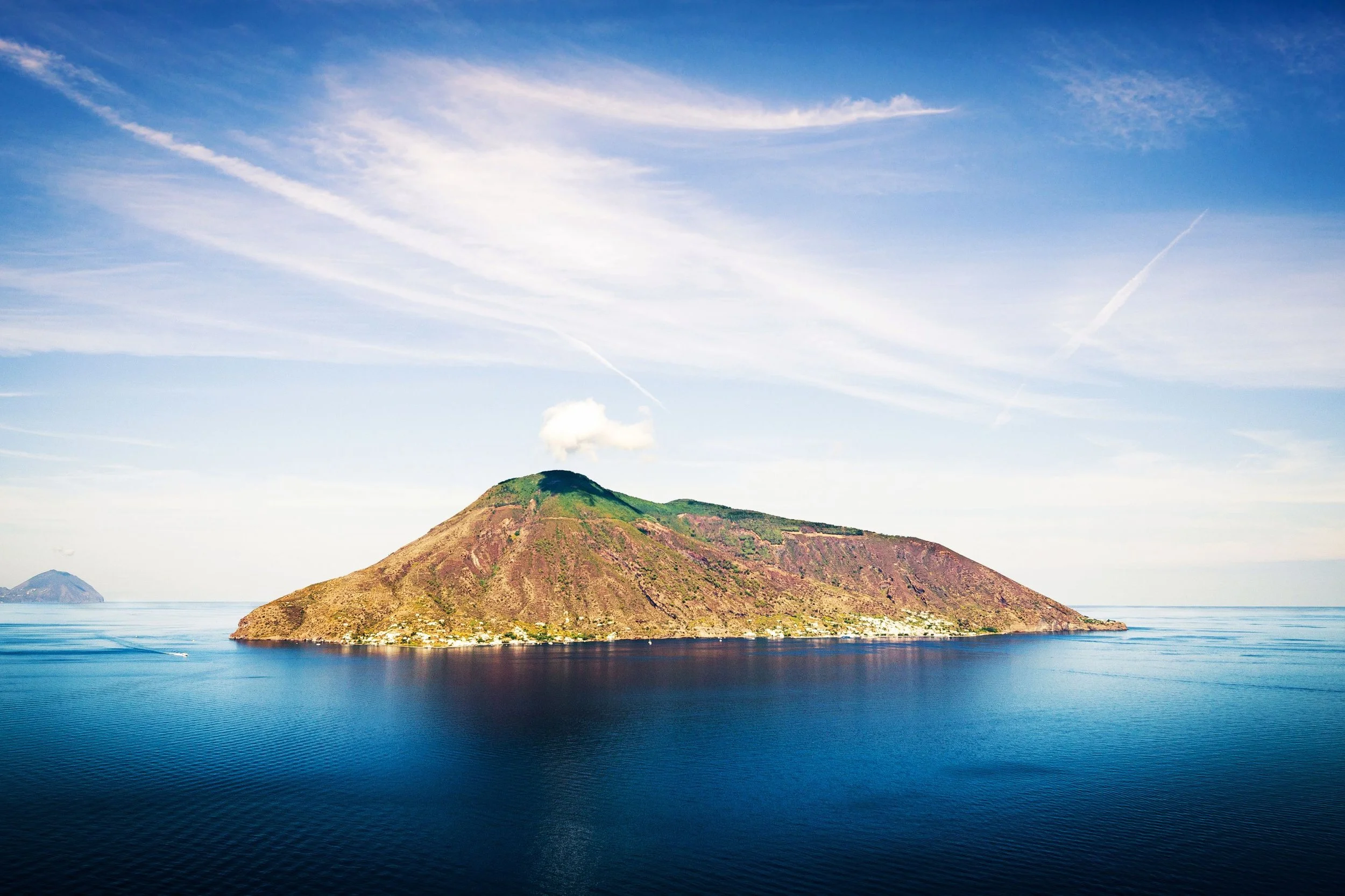 An island with a volcano in the ocean under a partly cloudy sky.