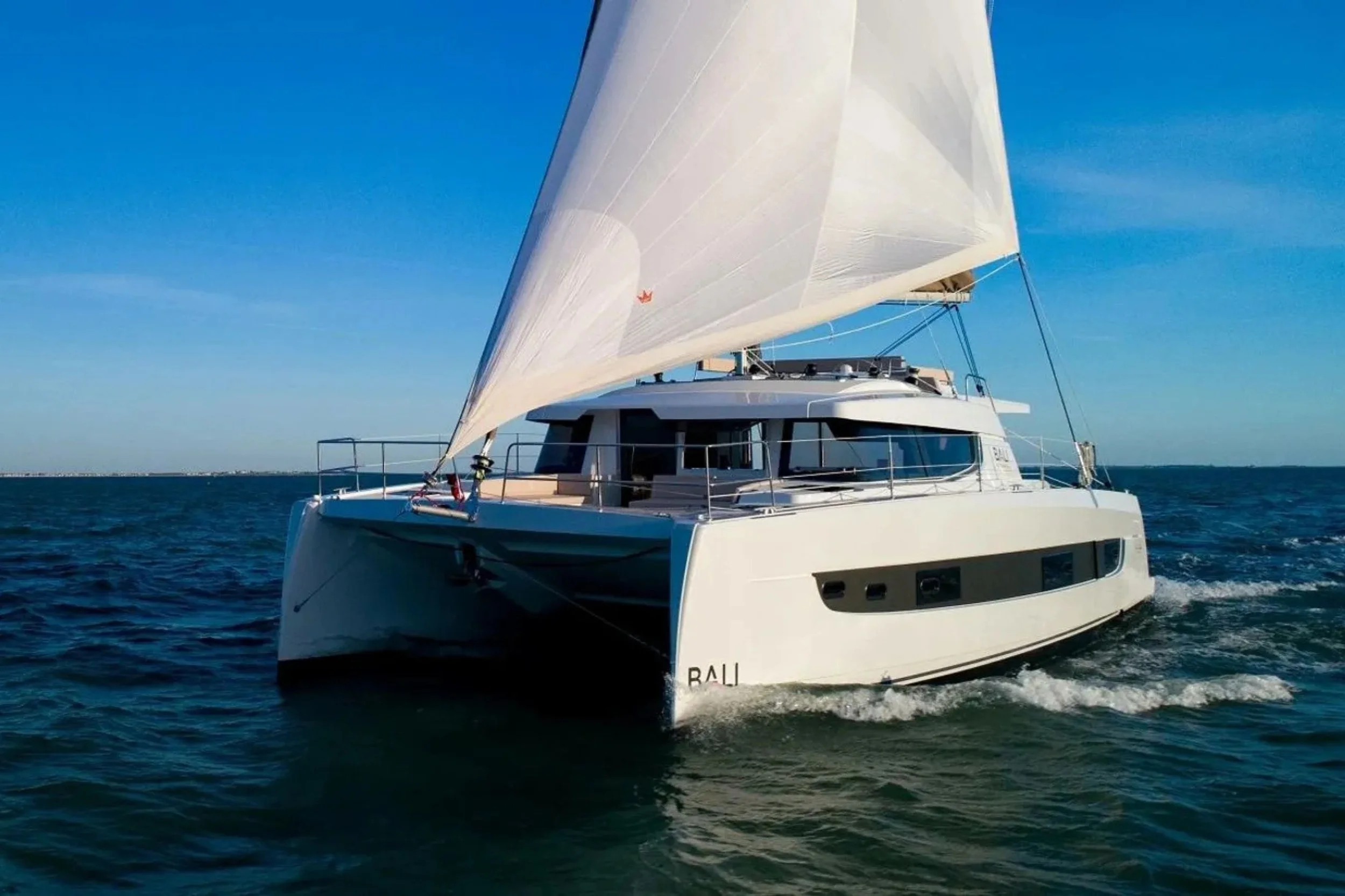 A white sailing yacht with large sails on the open water during daytime with clear blue skies.