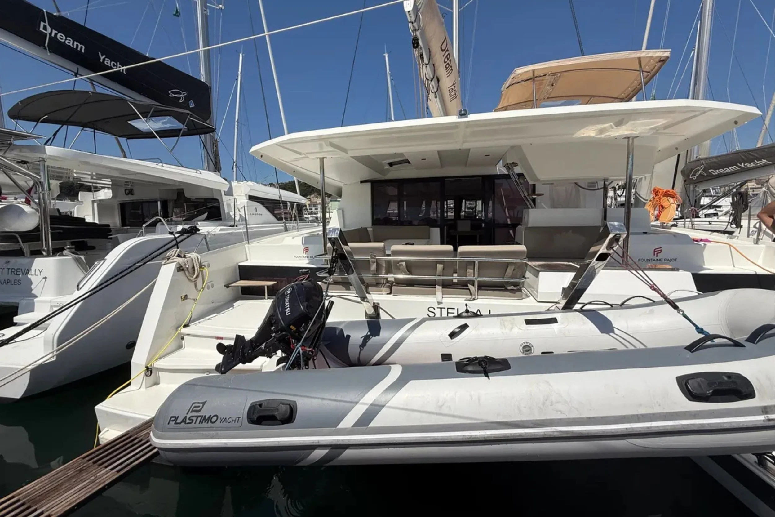 A white motor yacht docked at a marina, with other boats and sailboats nearby under a clear blue sky.
