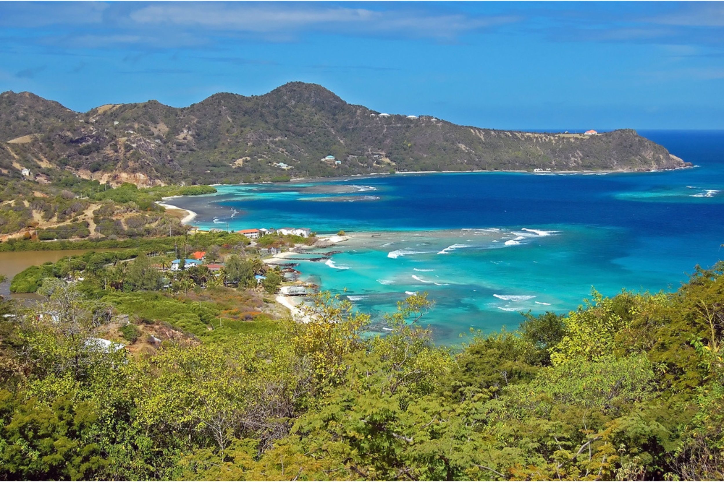 Colorful coastal landscape with turquoise ocean, sandy beaches, lush green vegetation, and rugged mountains under a partly cloudy sky.