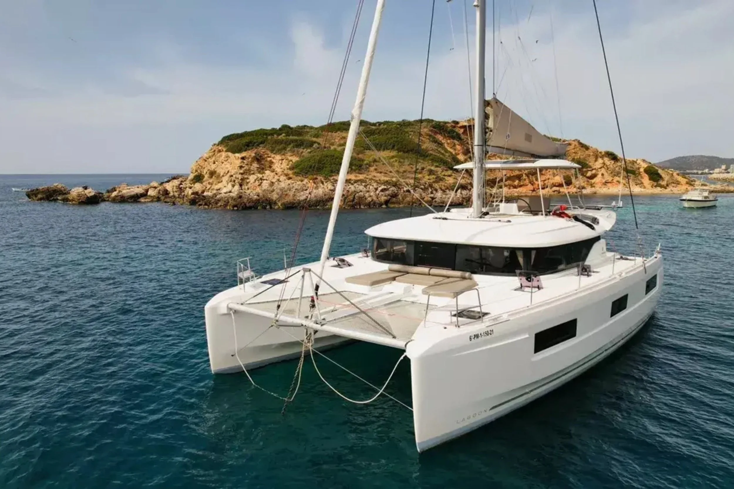 A white sailing yacht anchored near a rocky island with greenery.