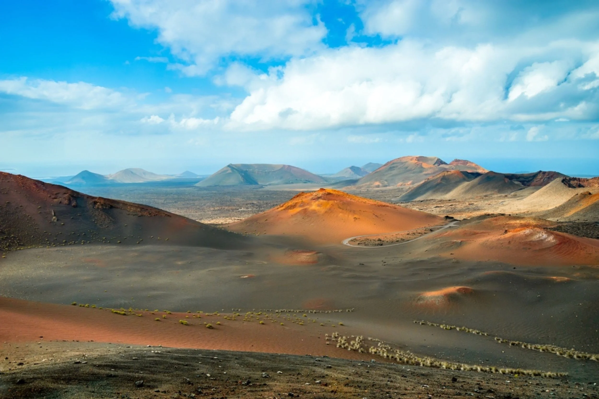 Scenic view of volcanic landscape with colorful volcanic hills, mountains in the distance, and a partly cloudy sky.