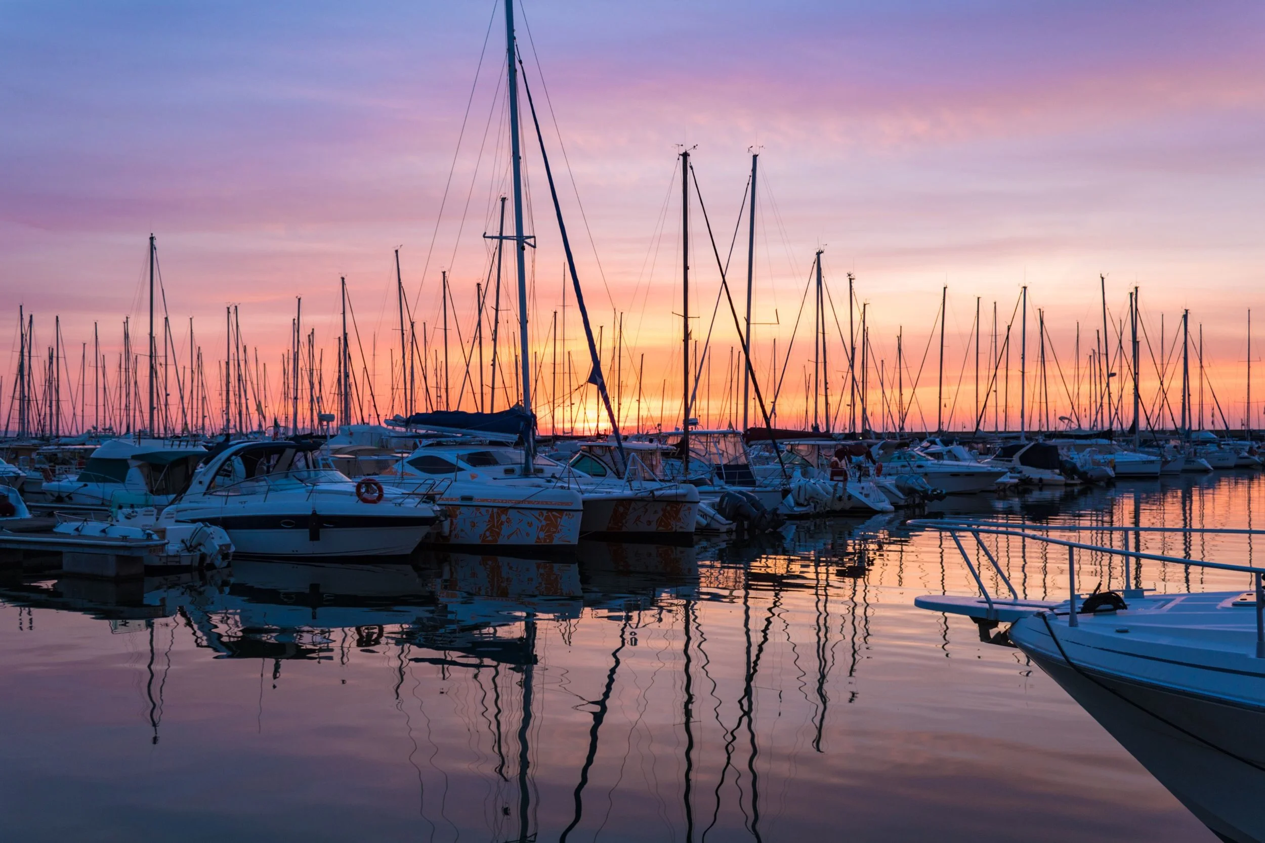 Boats docked at a marina during sunset with colorful sky and reflections in the water.