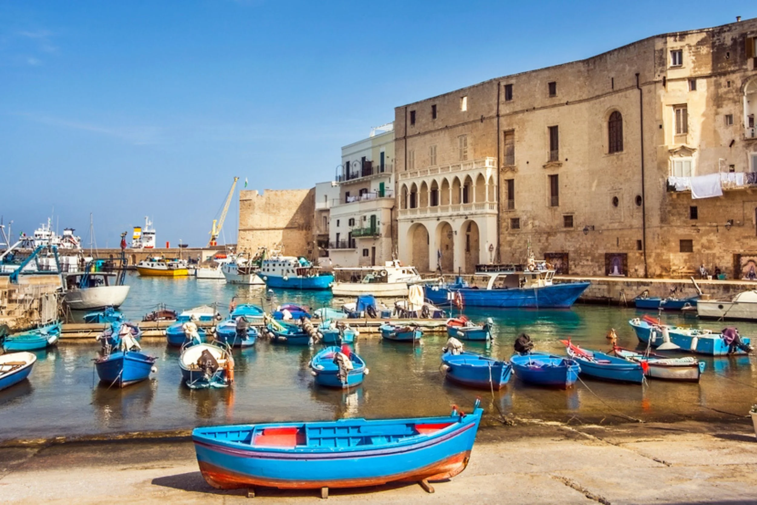 A harbor with boats docked in the water and historic buildings along the waterfront, with a clear blue sky overhead.